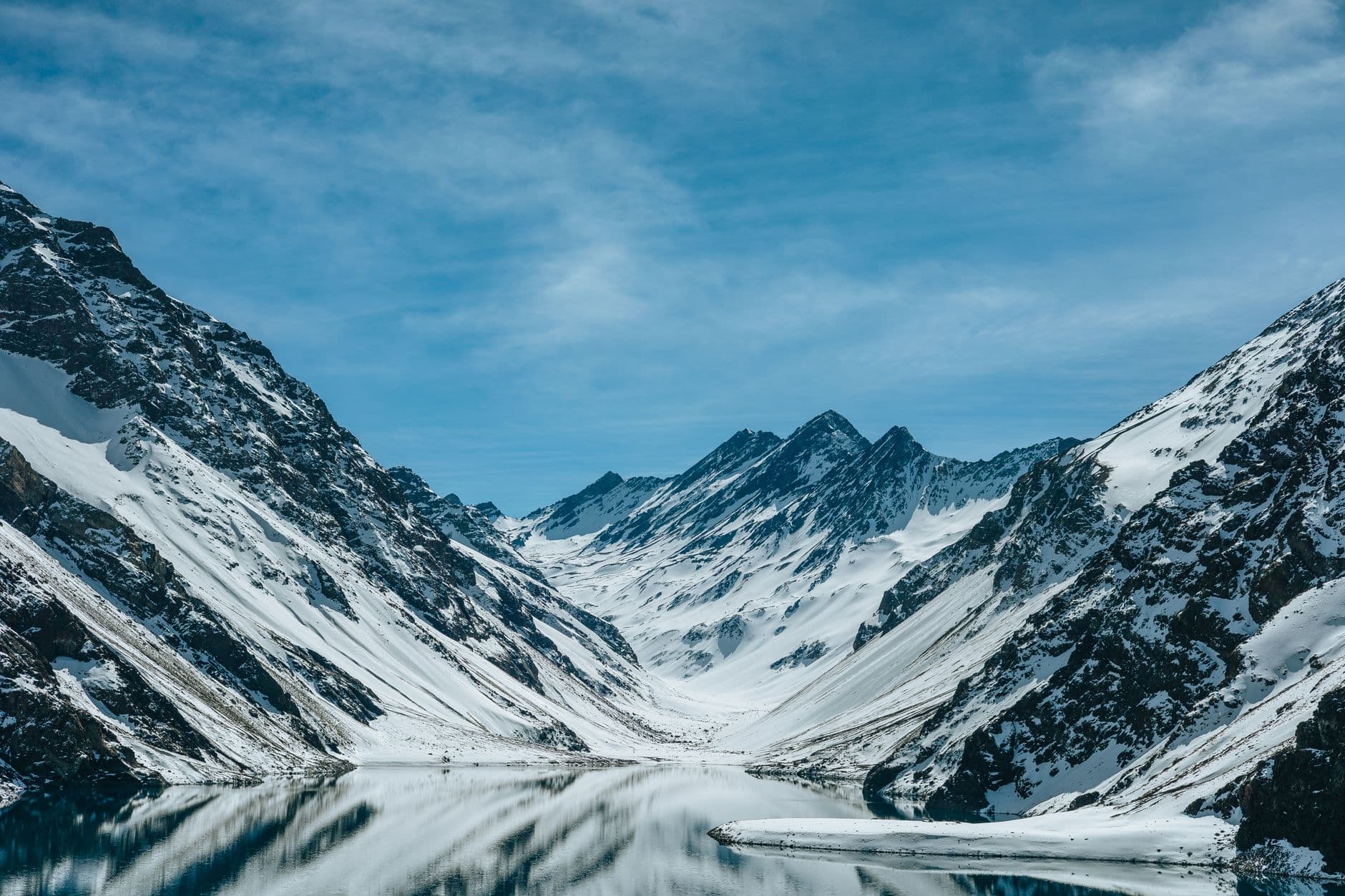 Peaceful winter scene of snow-capped mountains reflecting in a calm lake with a clear blue sky.