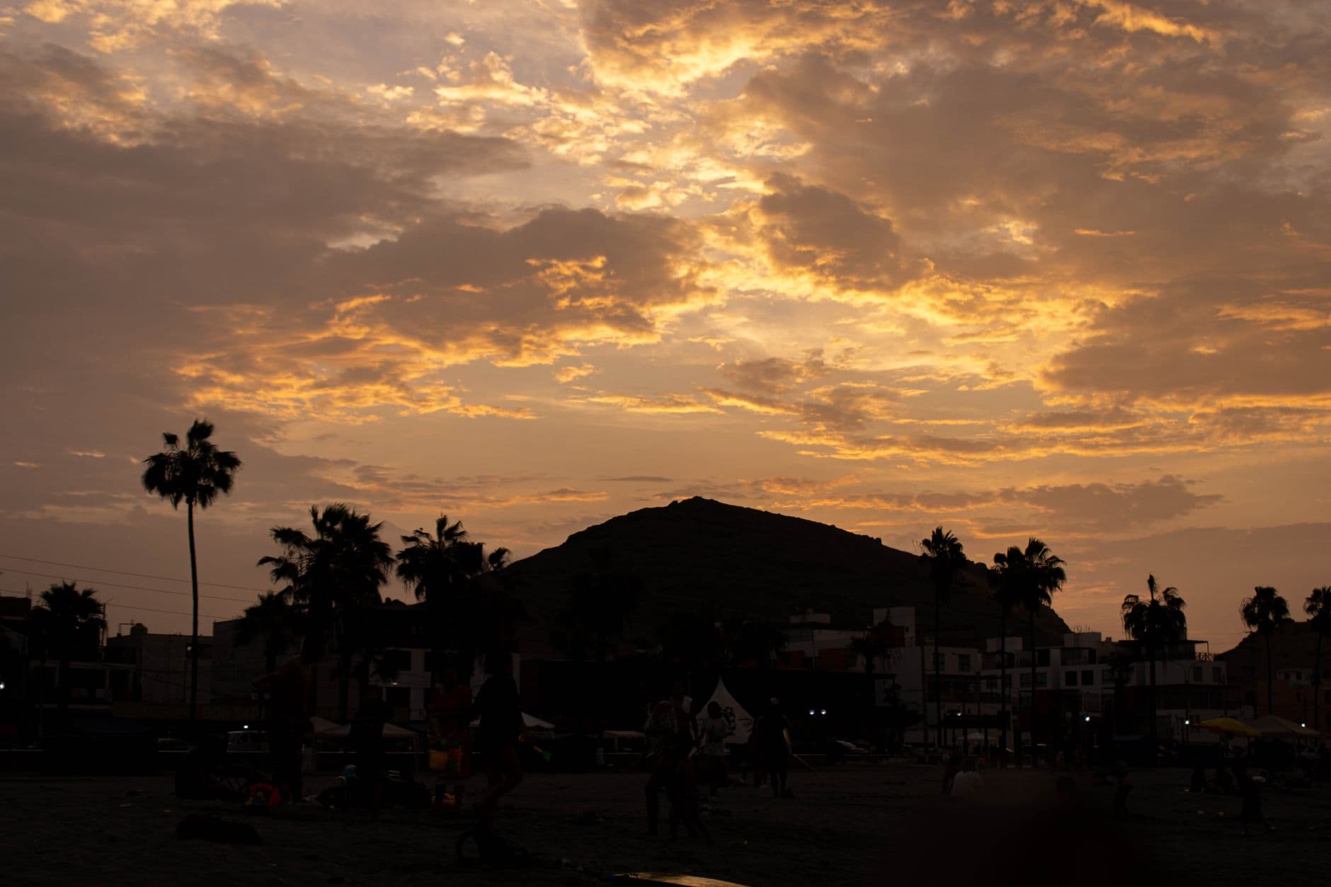 Scenic silhouette view of sunset over Cerro Azul, Peru, with palm trees and urban backdrop.