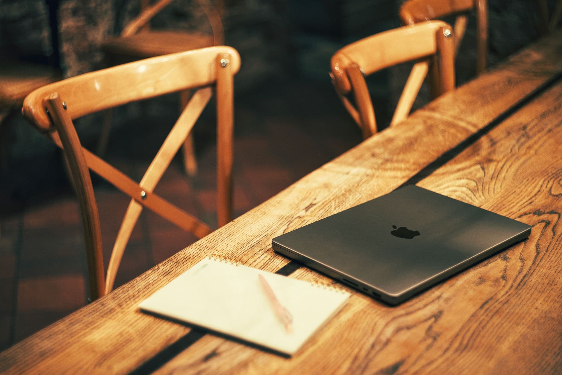 Warm setting of a wooden table with a laptop and notebook, ideal for working in a cozy environment.