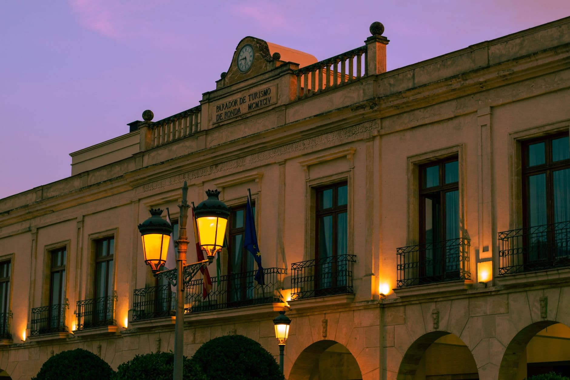 Elegant evening view of the Parador de Ronda with streetlights during dusk in Ronda, Spain.