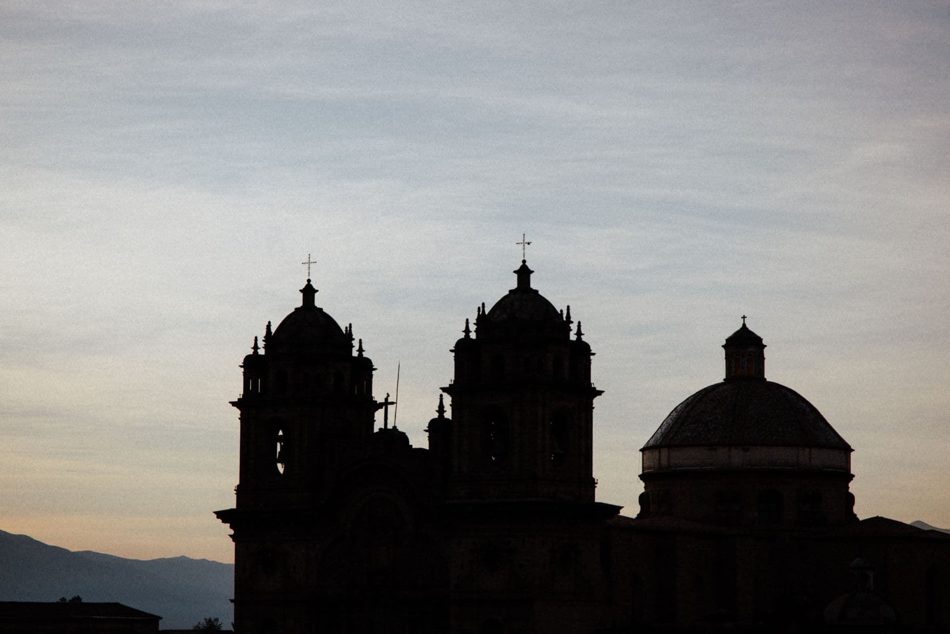 Silhouette of a historic church with domes and towers at dusk in Cusco, Peru.