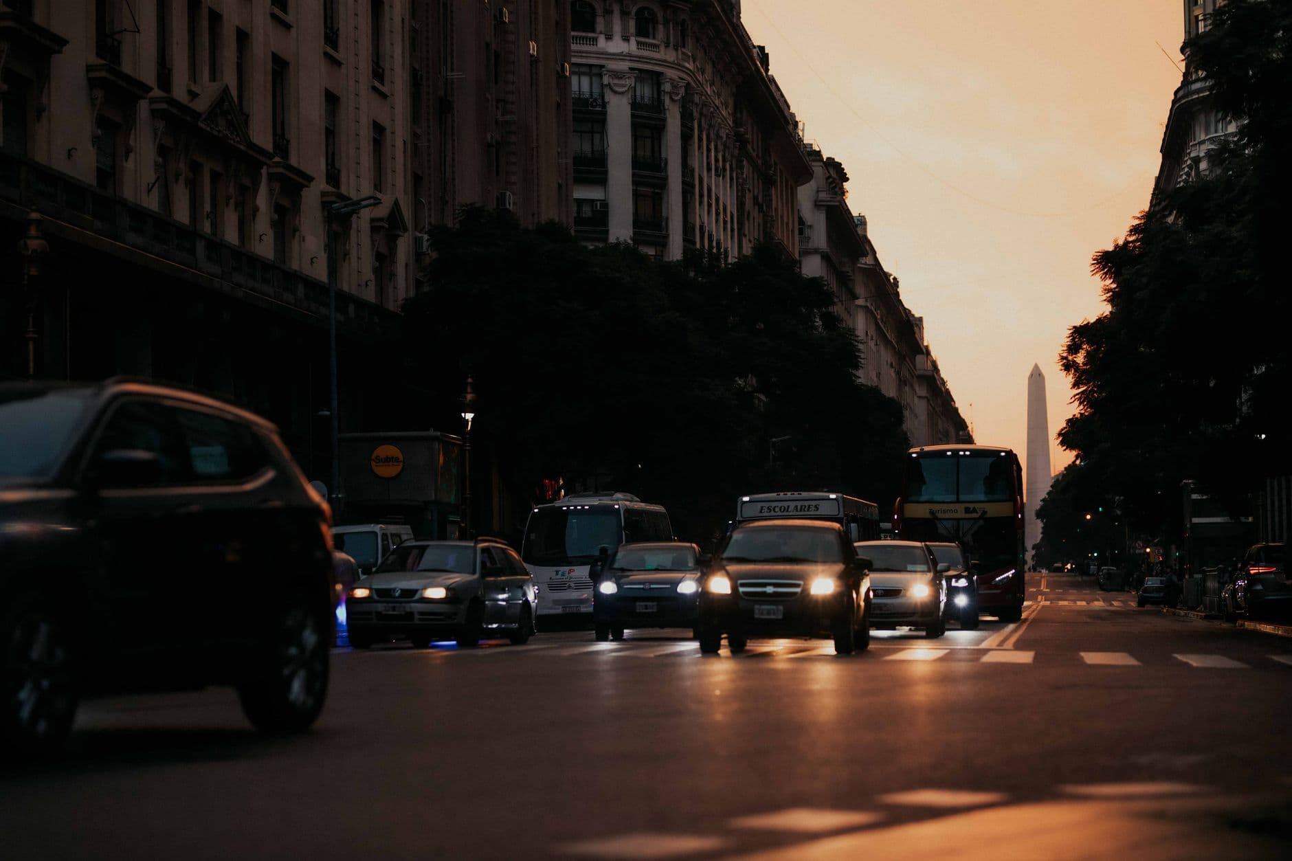 Traffic on a city street during sunset with city skyline and obelisk in the background.