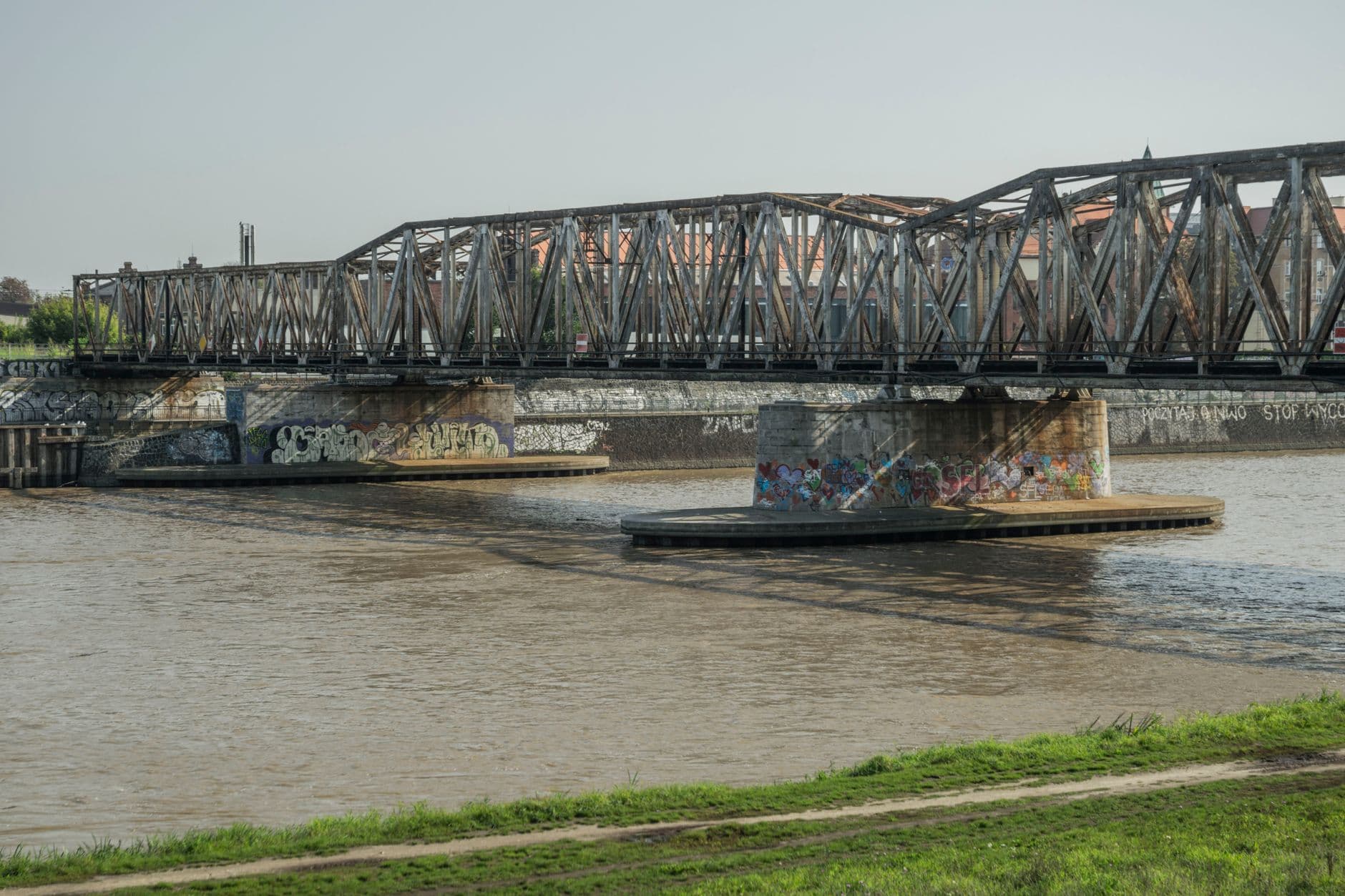 A steel bridge spans the Odra River in Wrocław, Poland, on a sunny day.