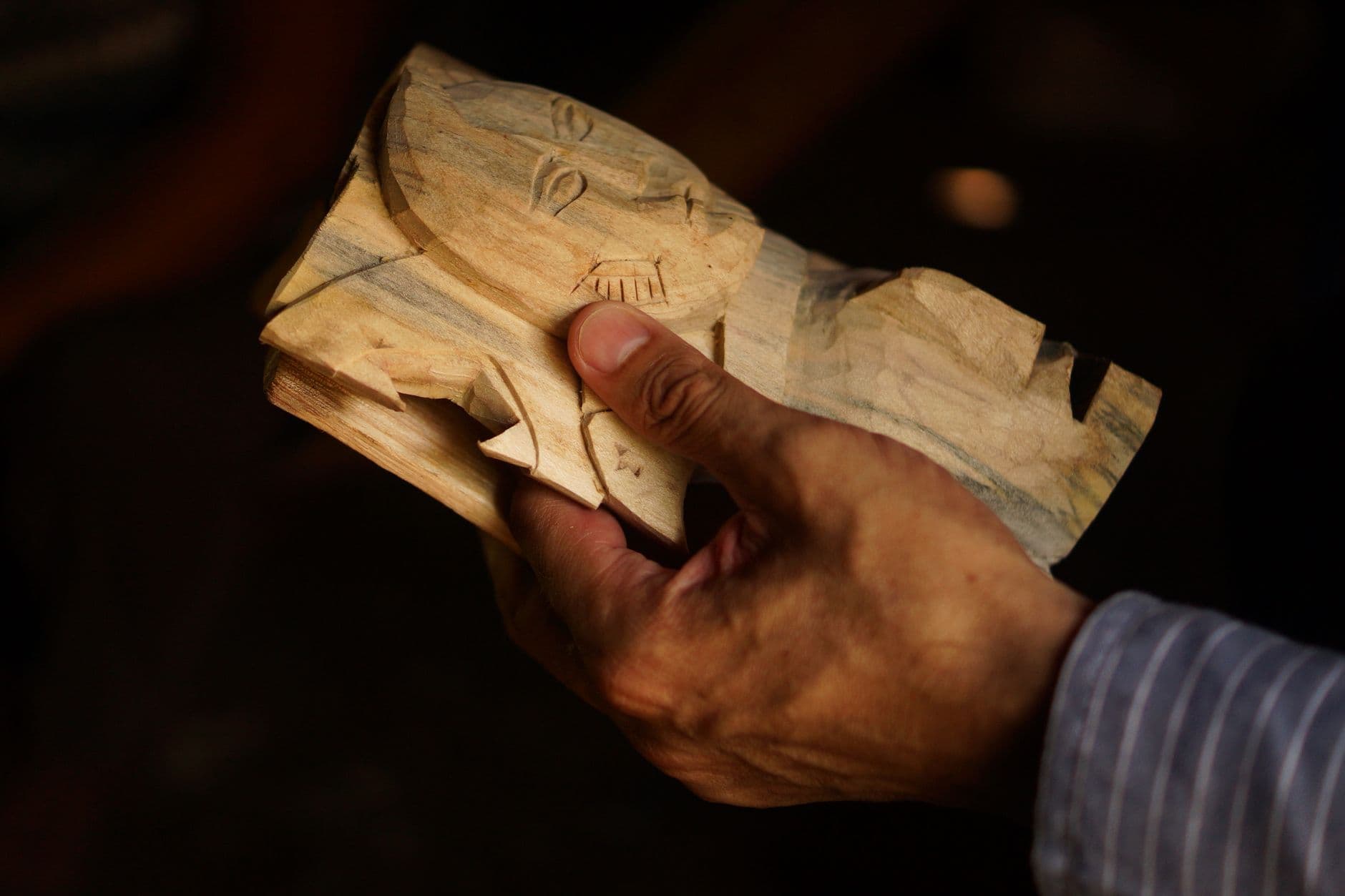 Artisan holding a handcrafted wooden mask in Yaxcabá, Mexico. Close-up shows detailed carving.