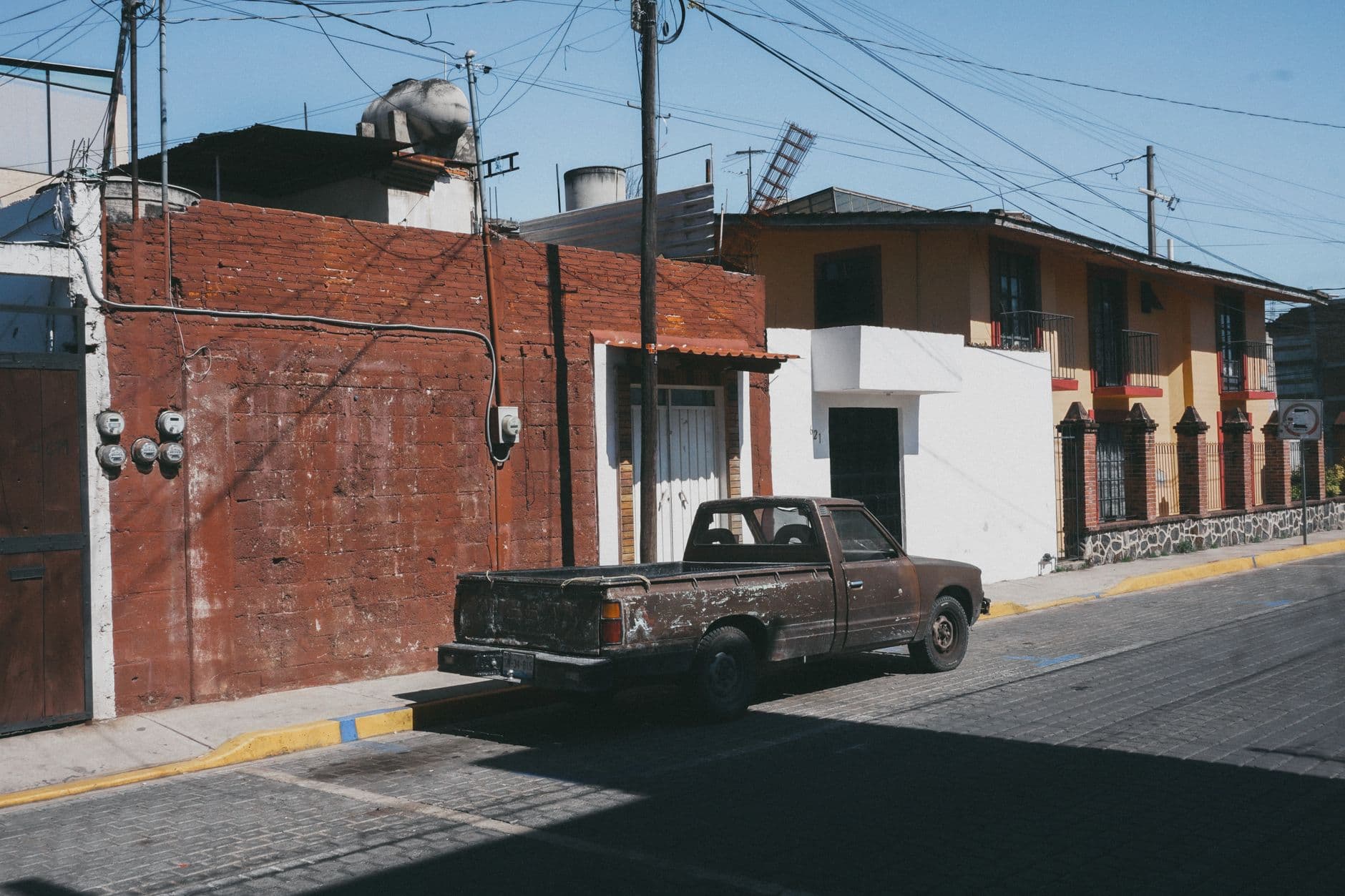 Old classic pickup truck parked along colorful urban street with rustic buildings.