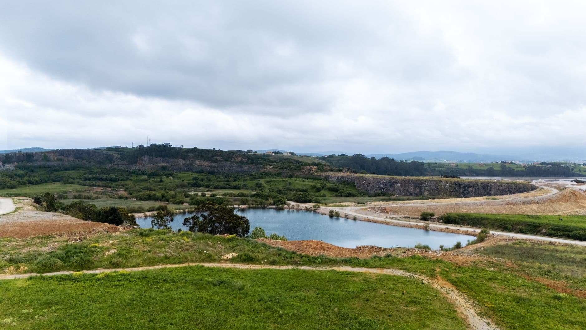 Aerial view of a quarry landscape with lush greenery and a serene water body in Cantabria, Spain.