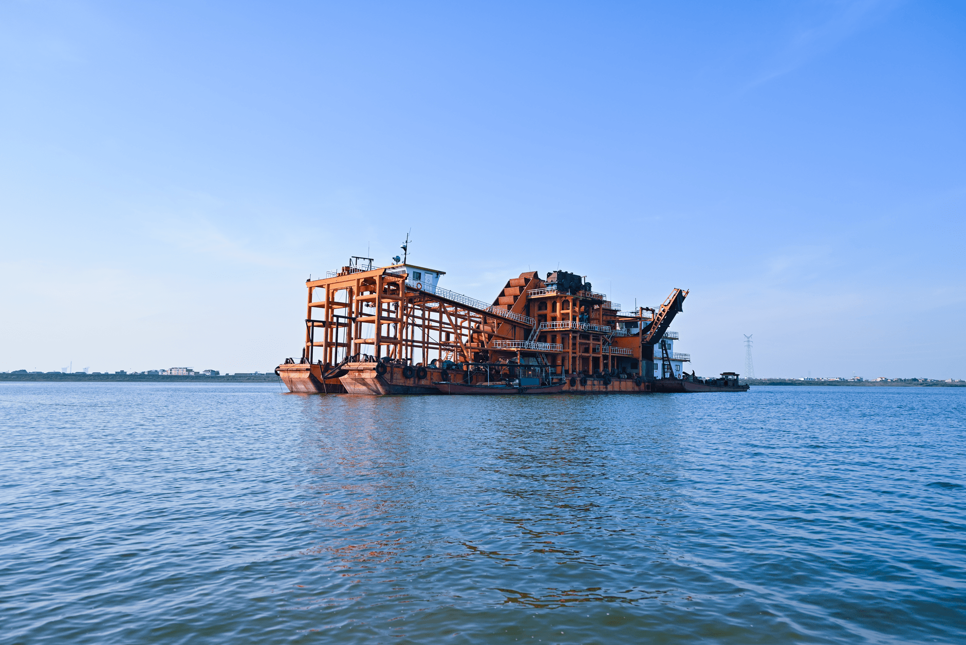 Rusty barge on calm water under a clear blue sky, showcasing industrial machinery.