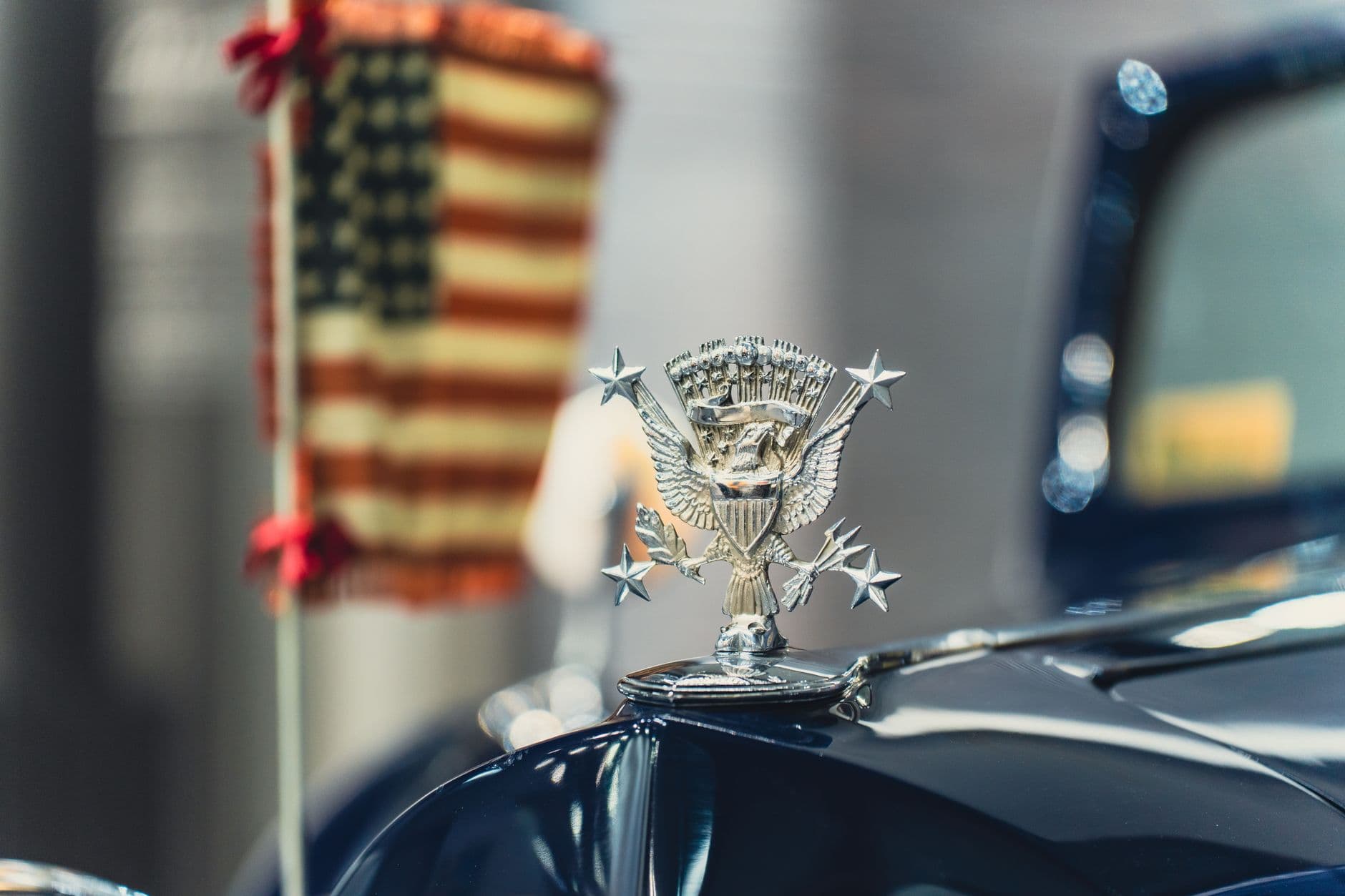 Classic car hood ornament with an American flag in the background, symbolizing vintage Americana.