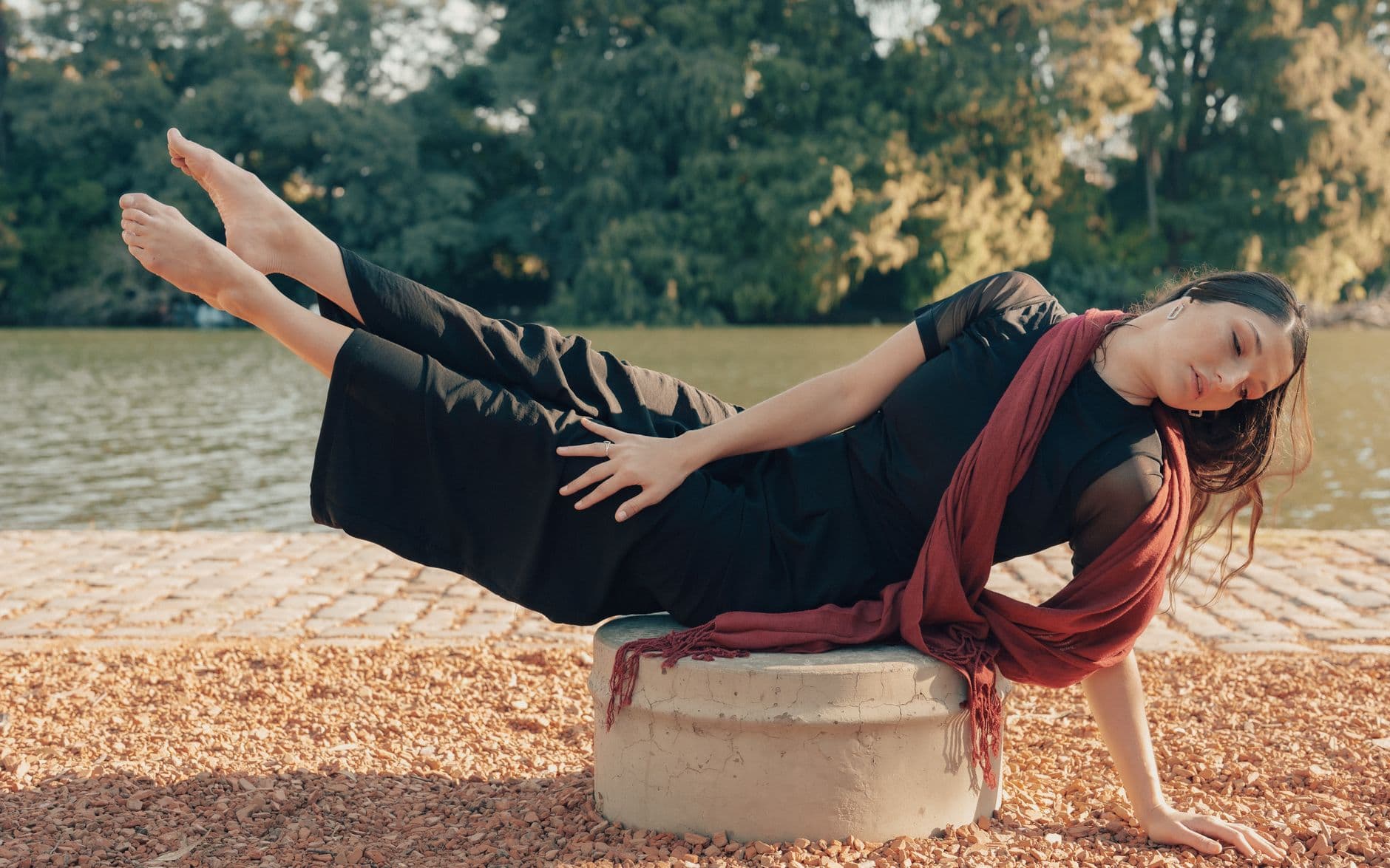 A woman in a graceful pose by a lake in Buenos Aires, wrapped in a red scarf with a serene expression.