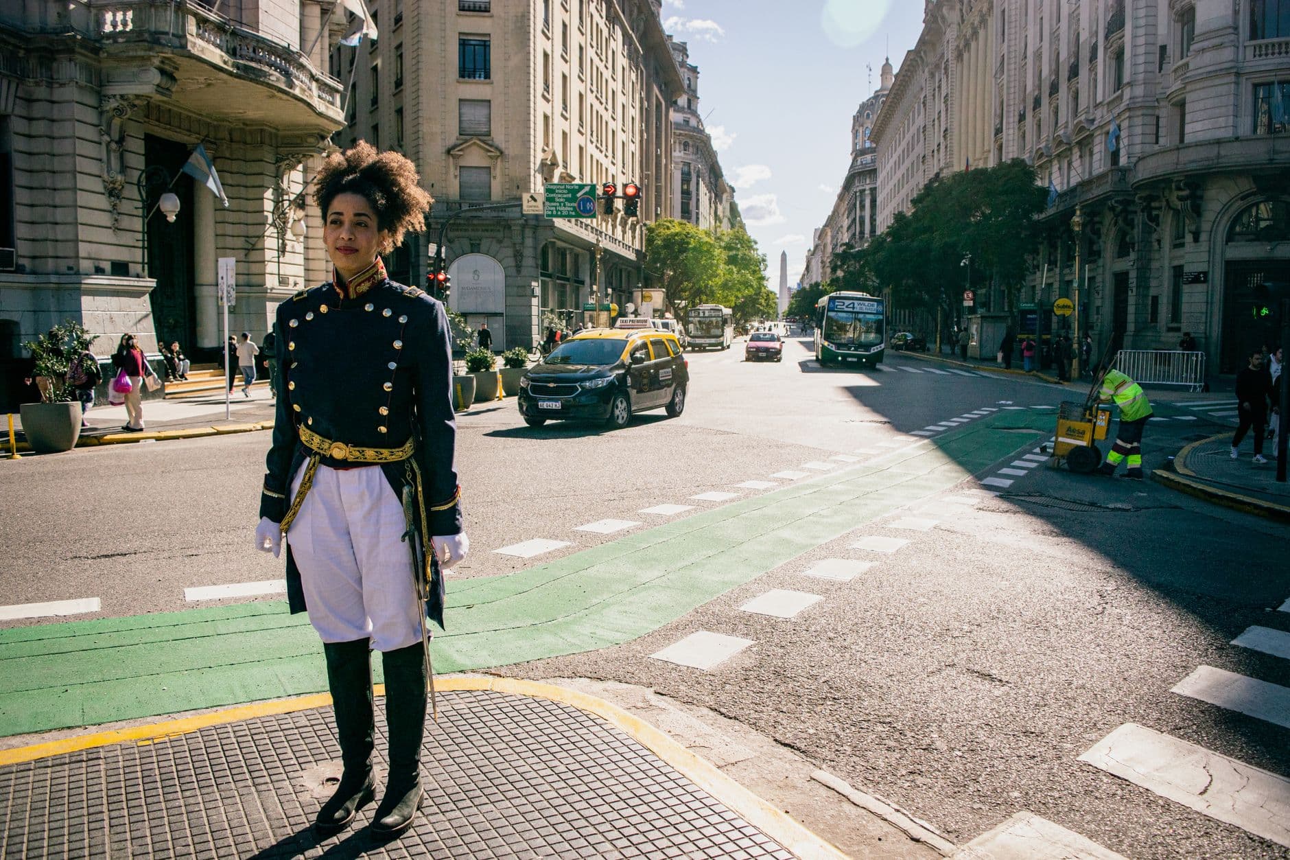 Person in colonial outfit standing on bustling Buenos Aires street with landmark view.