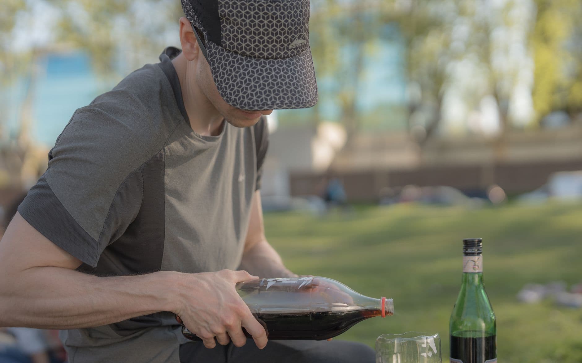 A young man in a park pours a beverage into a glass, enjoying a day outdoors.