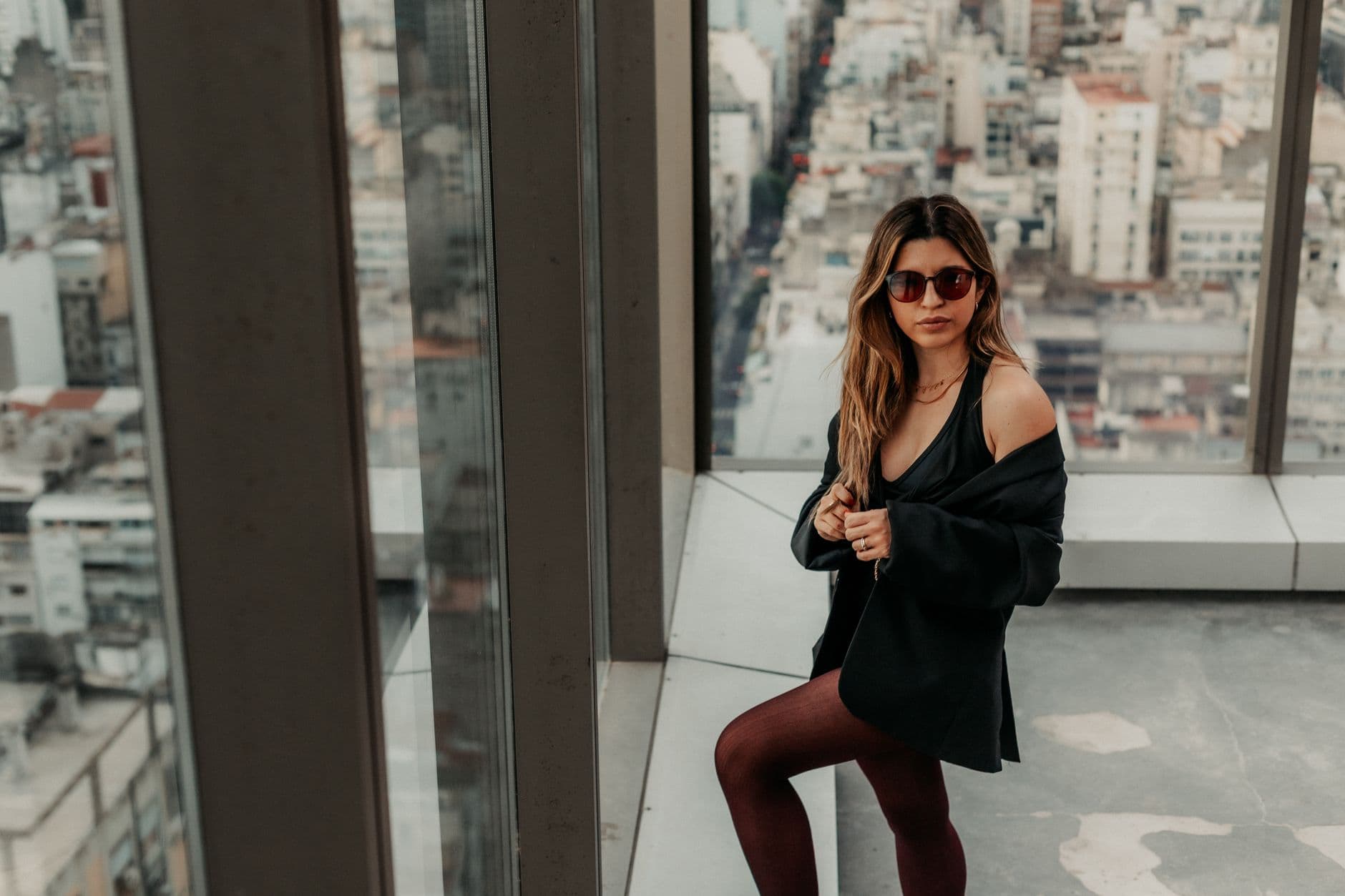 Woman in sunglasses poses in a high-rise apartment with a view of Buenos Aires skyline.
