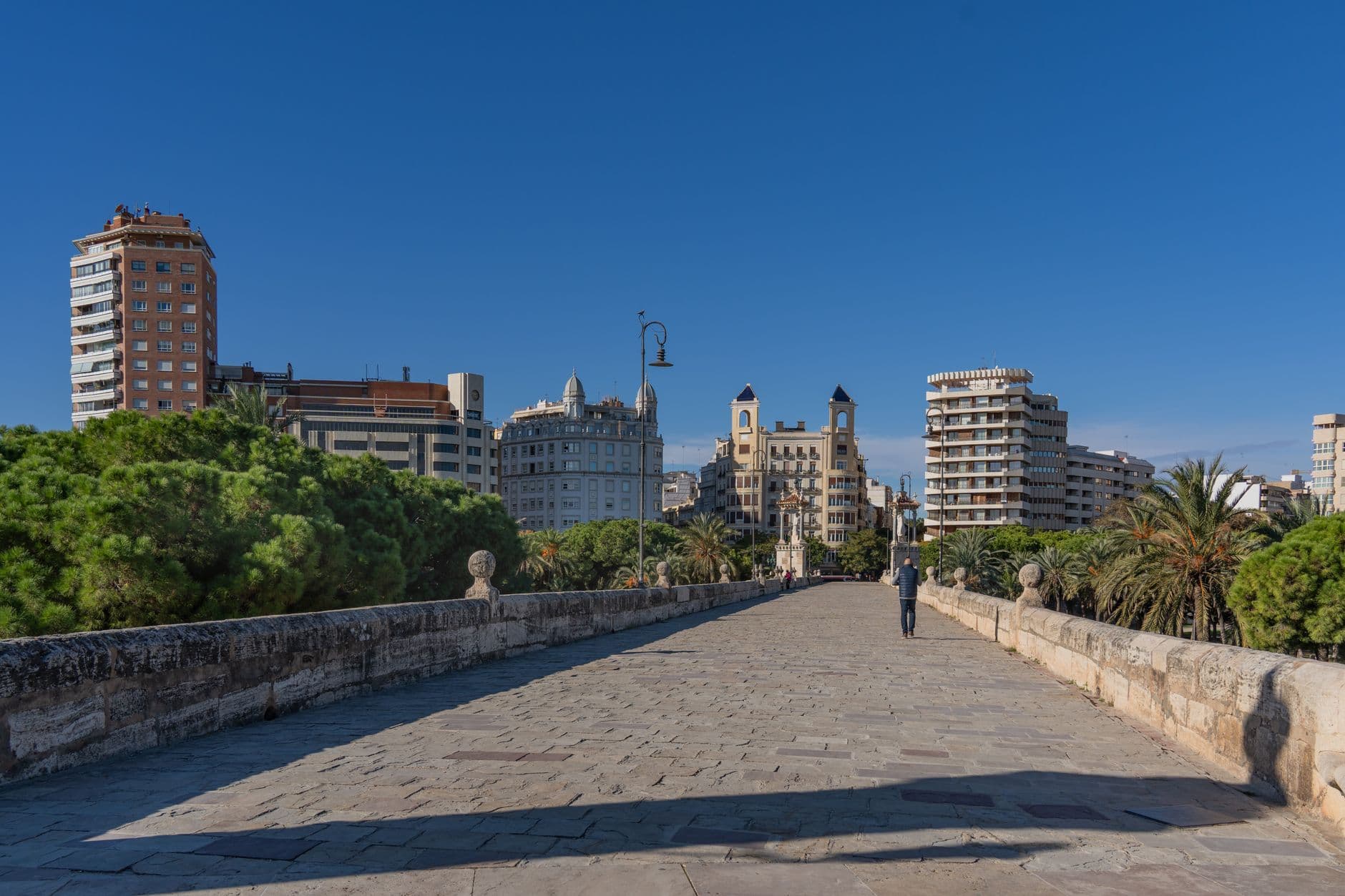 View of Valencia's skyline from a historic stone bridge on a sunny day, with clear blue skies.