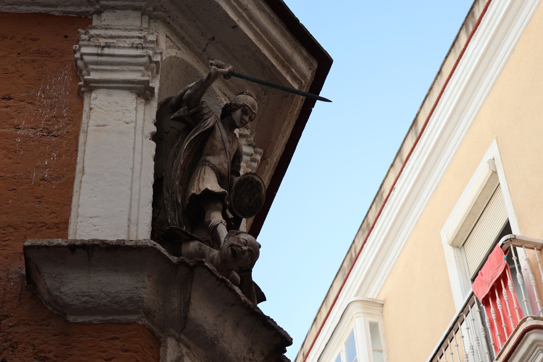 A detailed sculpture of Saint Michael hangs on a building facade in Cádiz, Spain.