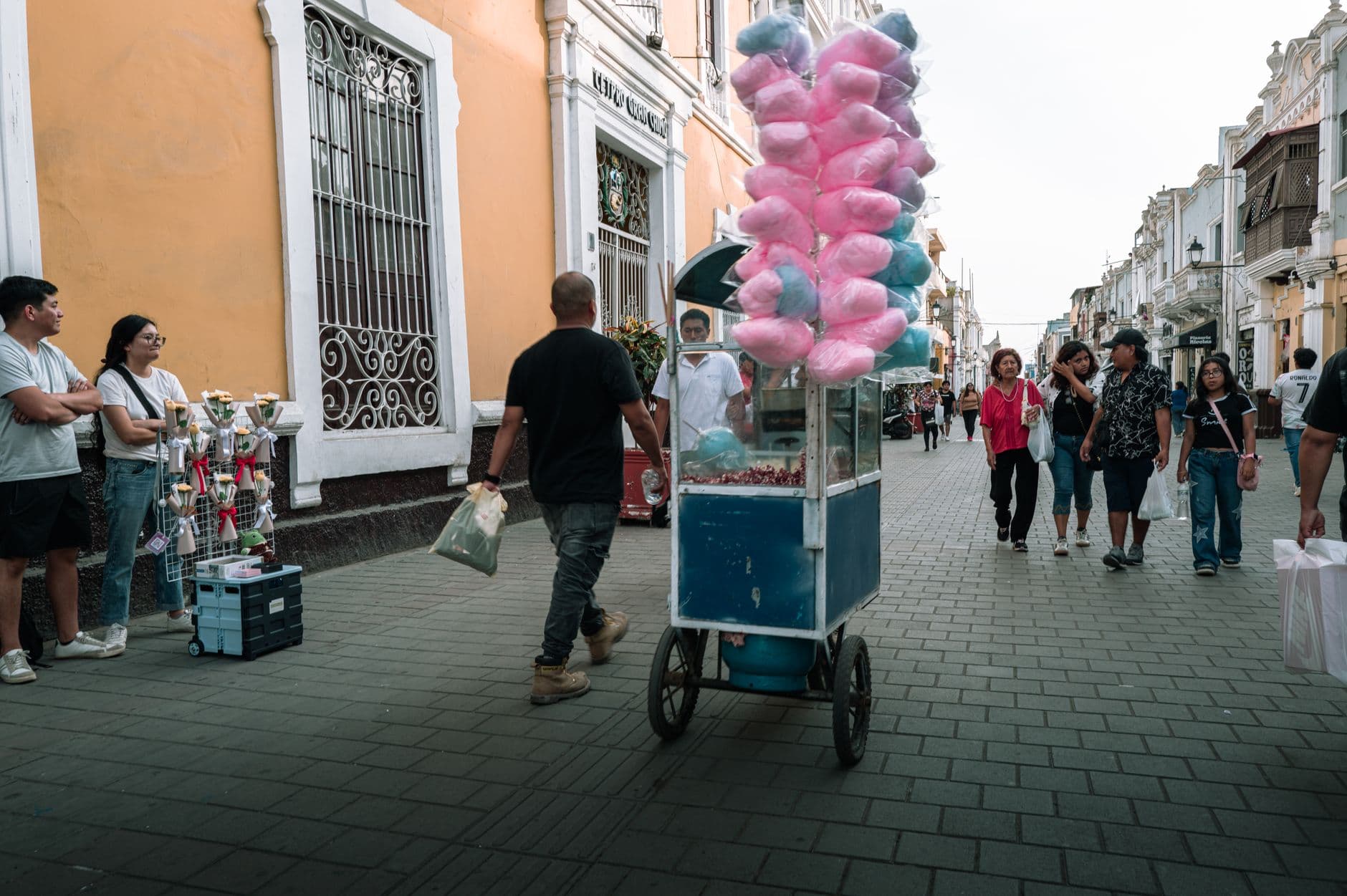 A vibrant street in Trujillo with a cotton candy vendor and passersby enjoying a sunny day.