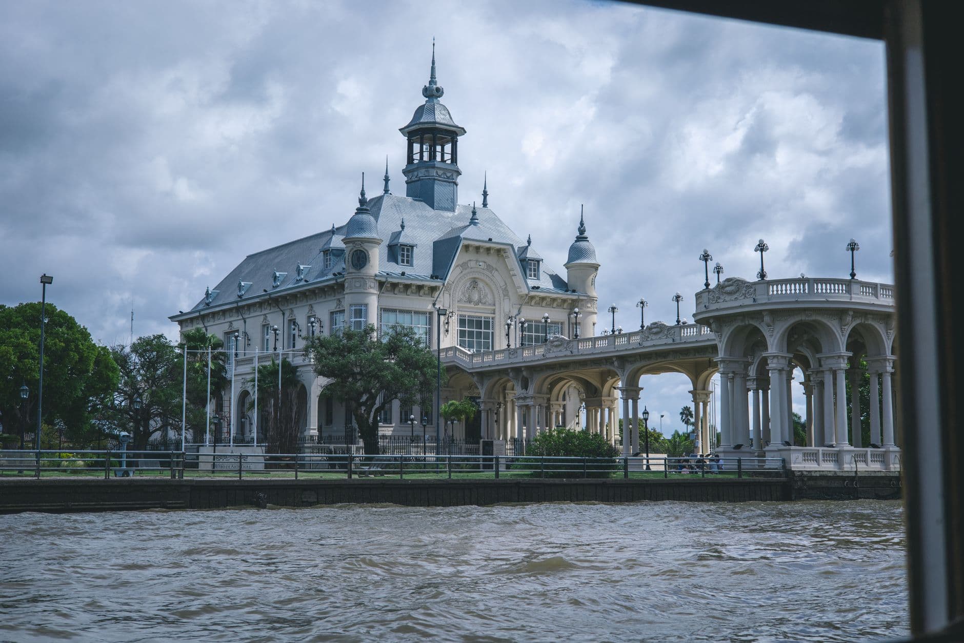 Elegant historic architecture of the Tigre Art Museum seen from across the river under cloudy skies.