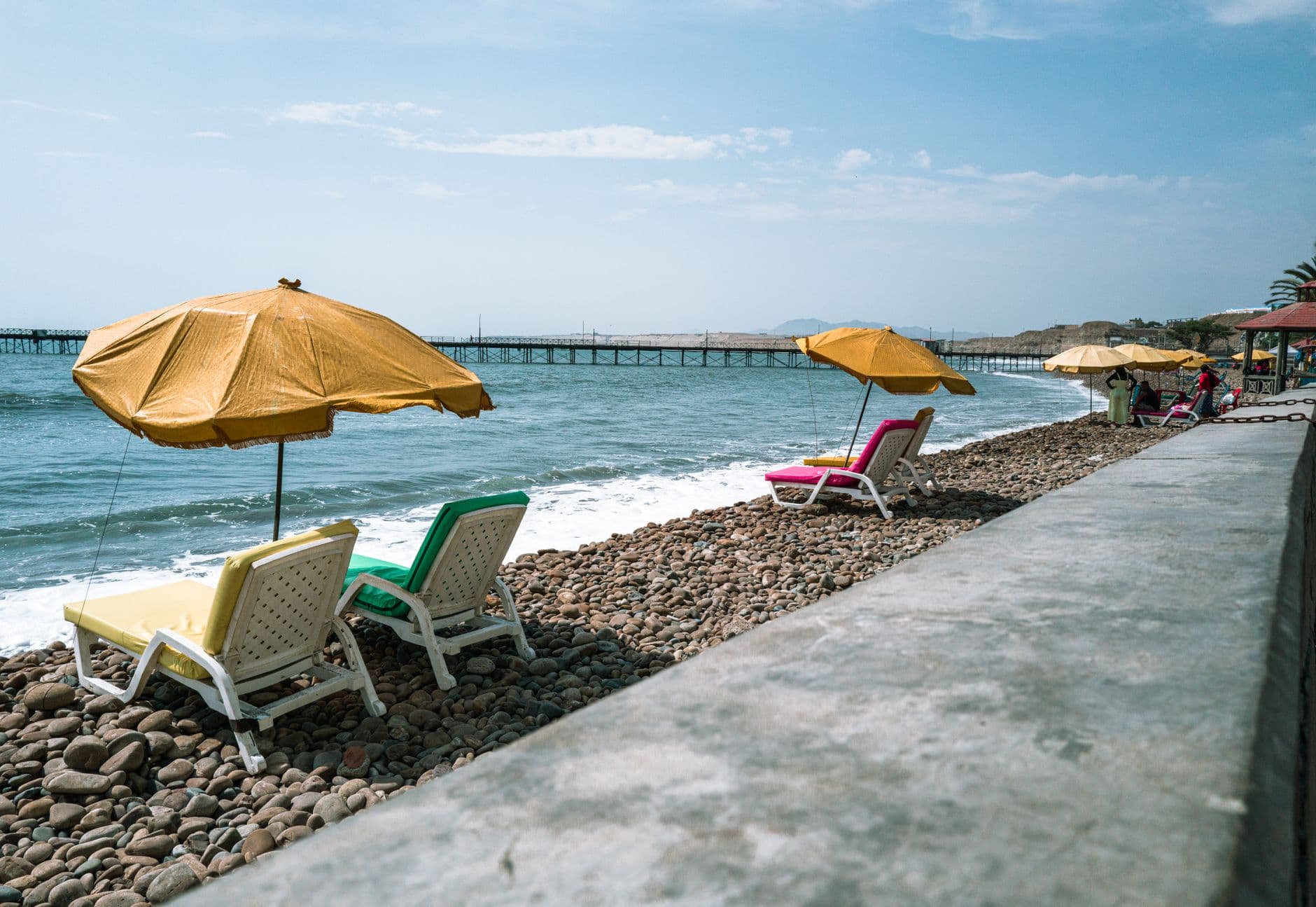 Relaxing view of colorful loungers and umbrellas on a pebble beach in Pacasmayo, Peru.