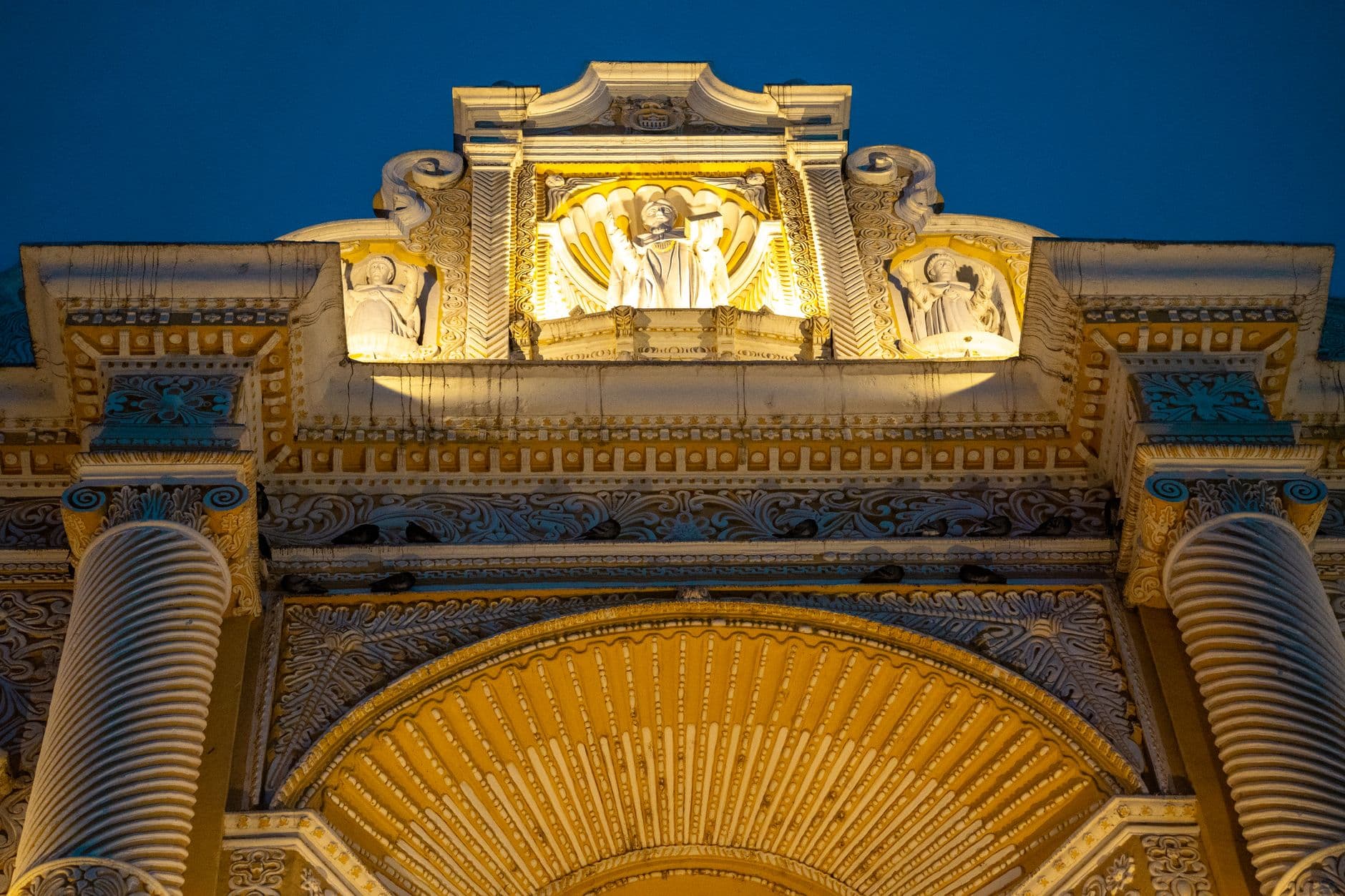 Close-up view of ornate architectural facade with evening illumination highlighting detailed sculptures.