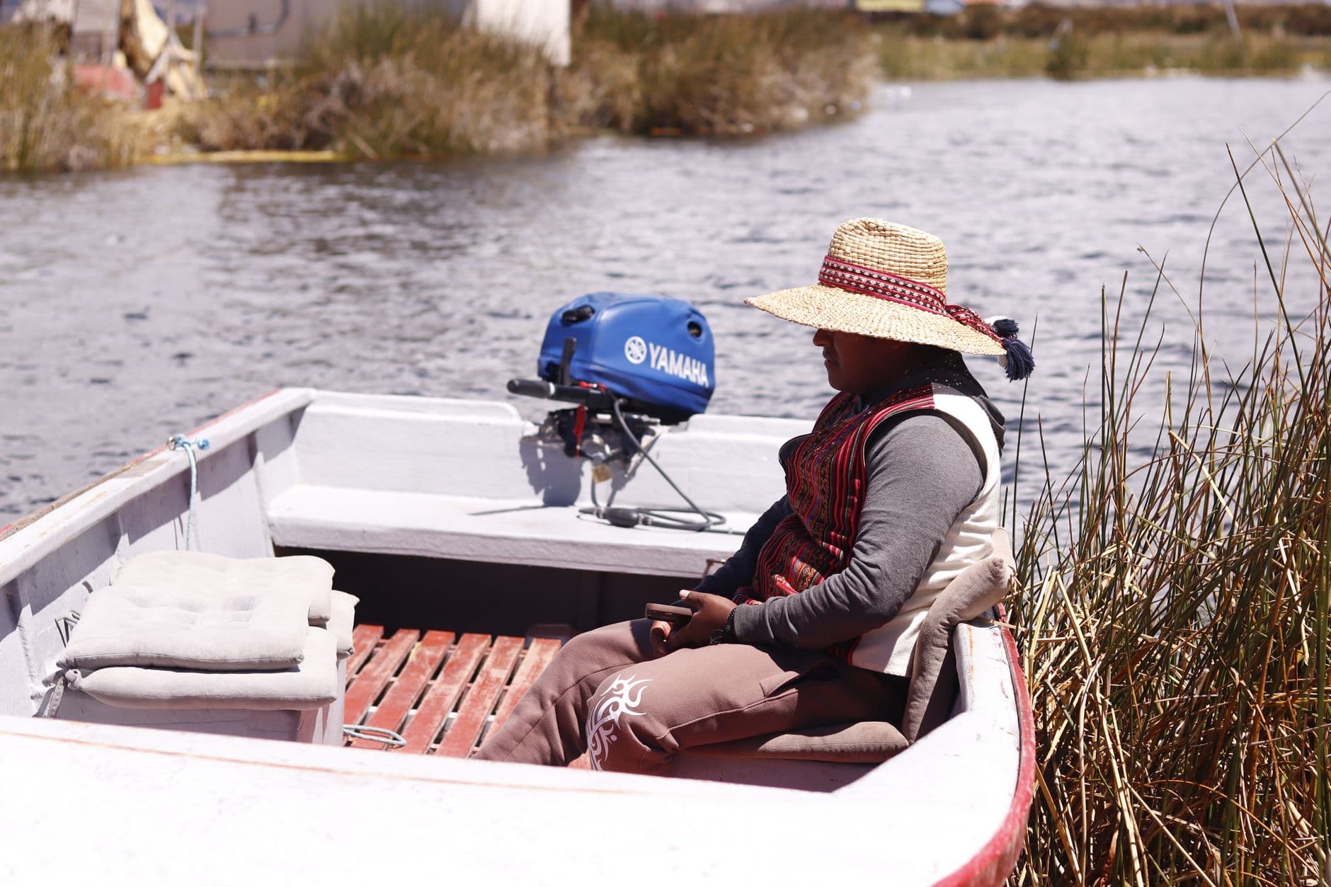 A person sitting in a boat on Lake Titicaca, wearing a straw hat, near Puno, Peru.