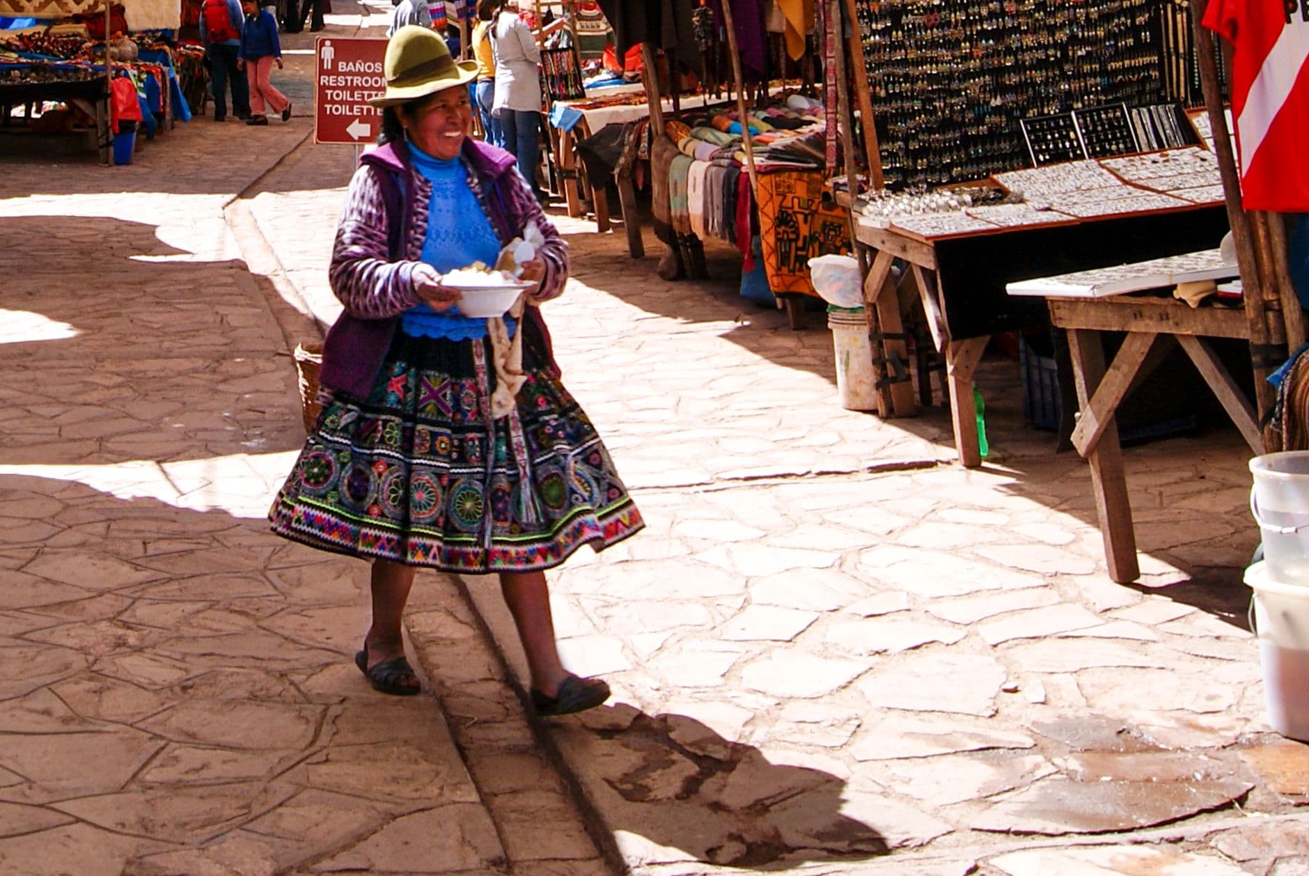 A woman in vibrant traditional attire walks through a bustling market in Cusco, Peru, showcasing cultural richness.