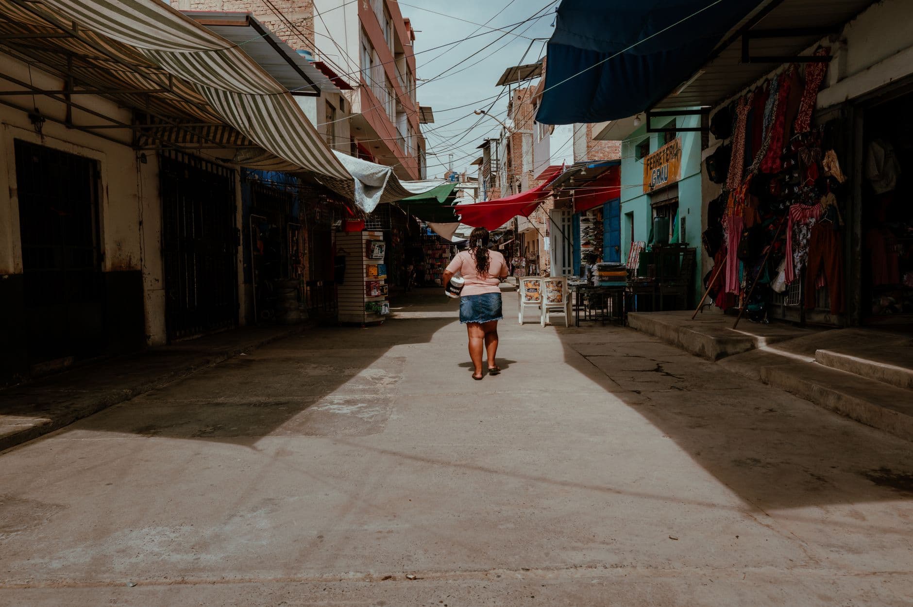 A person walks through a lively street market in Pacasmayo, Peru, under colorful awnings.