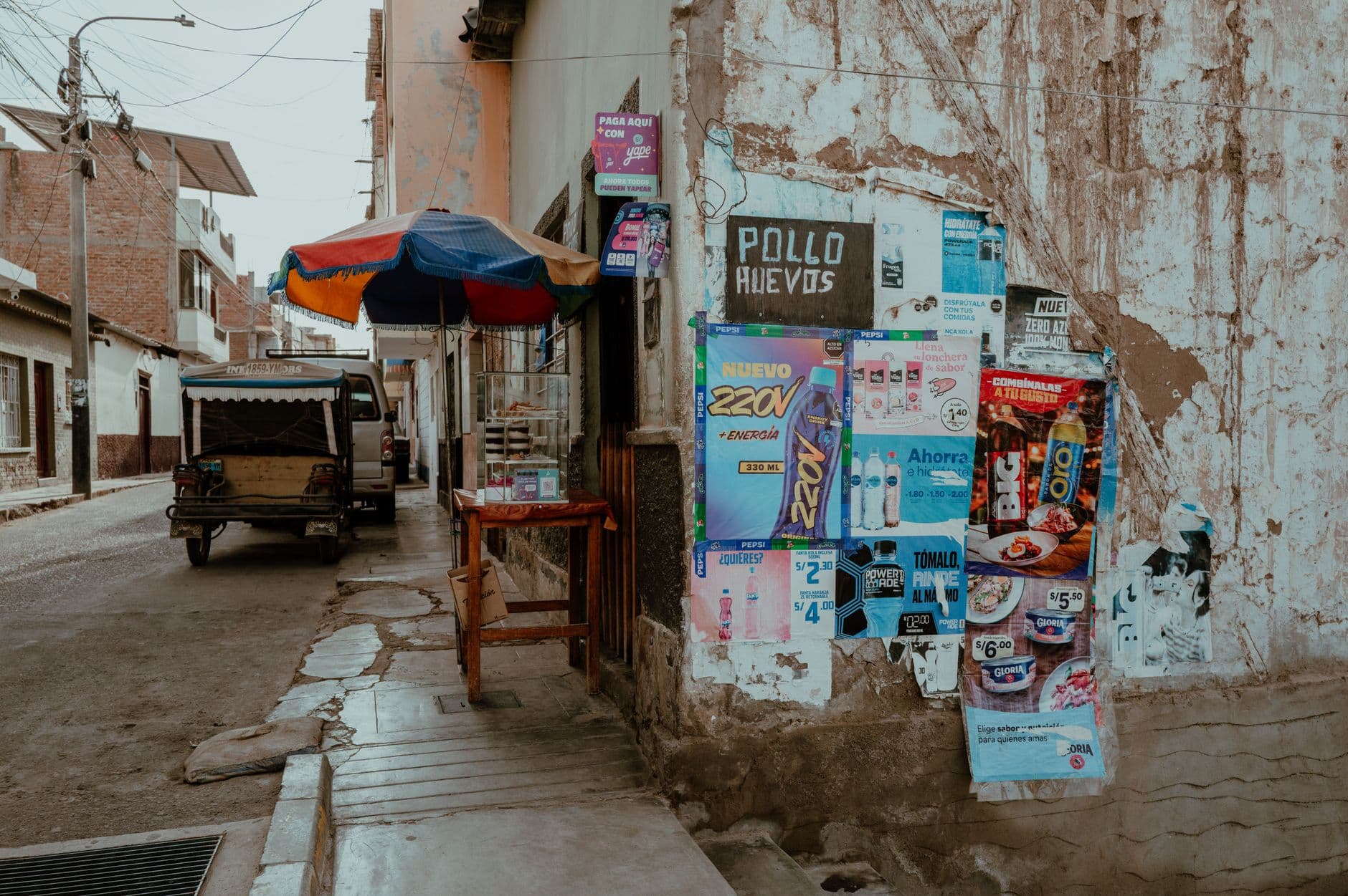 A vibrant street corner in Pacasmayo, Peru displaying local posters and a colorfully shaded stand.