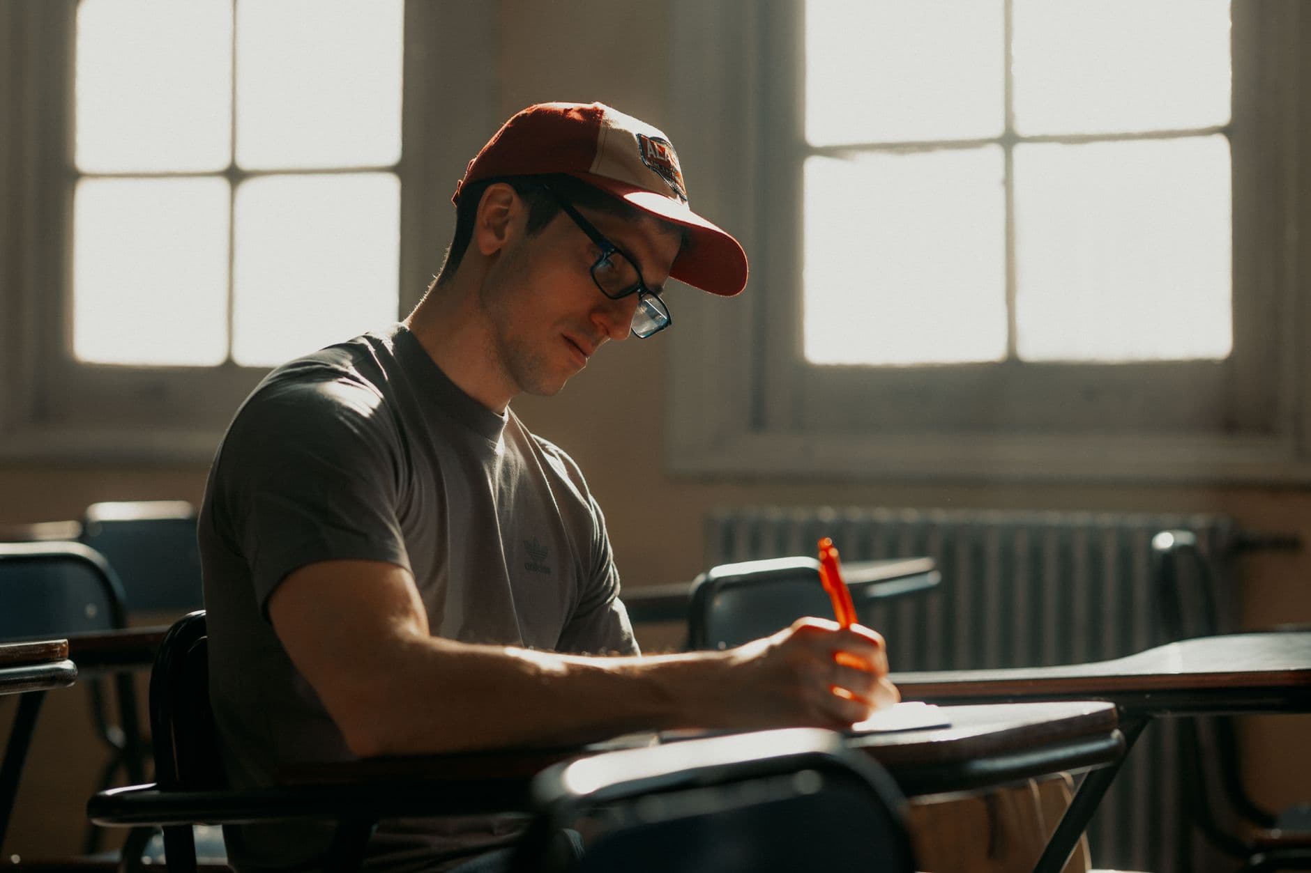 A student in a sunlit classroom concentrating on notes with a pen.
