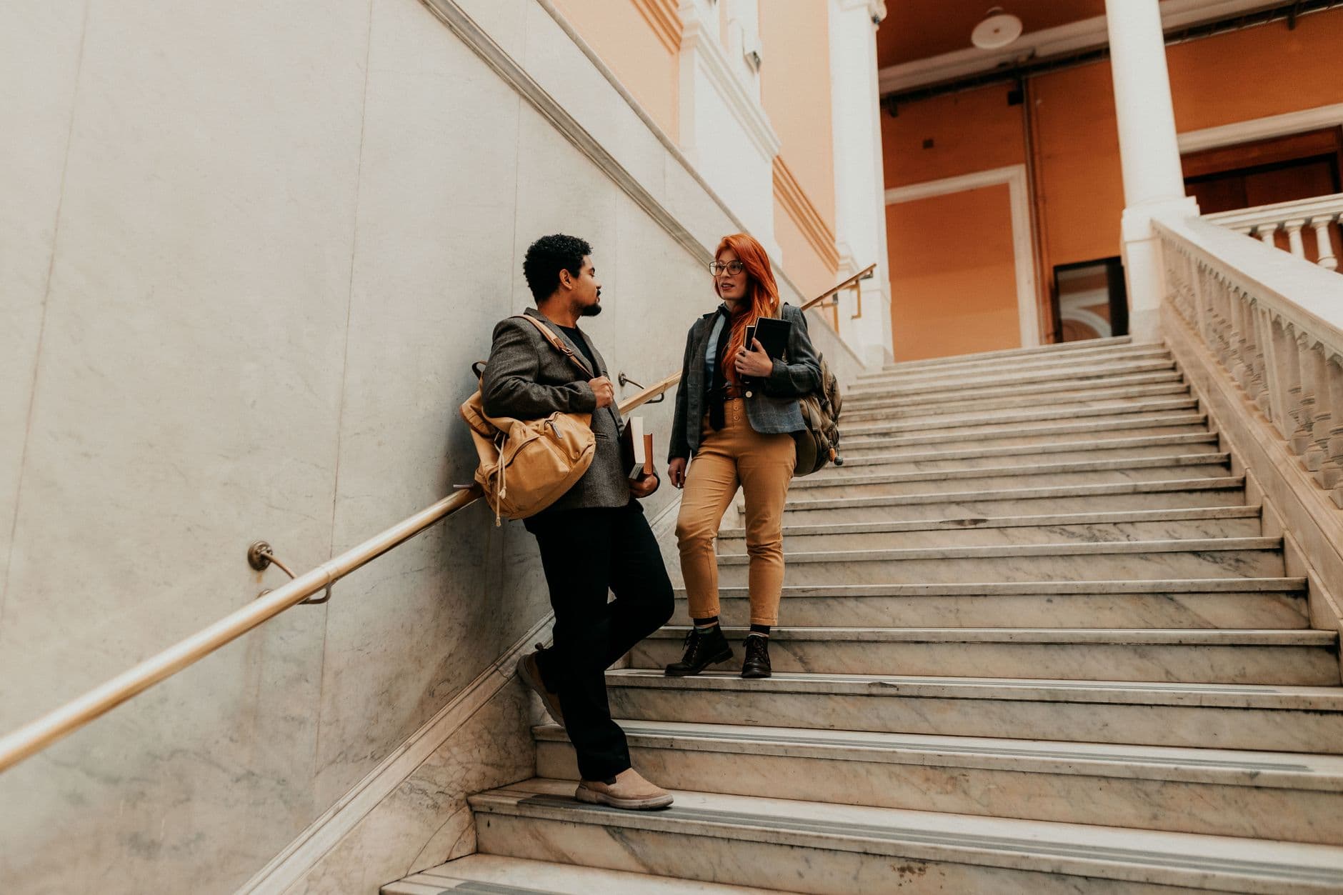 Two university students chat on a grand staircase indoors.