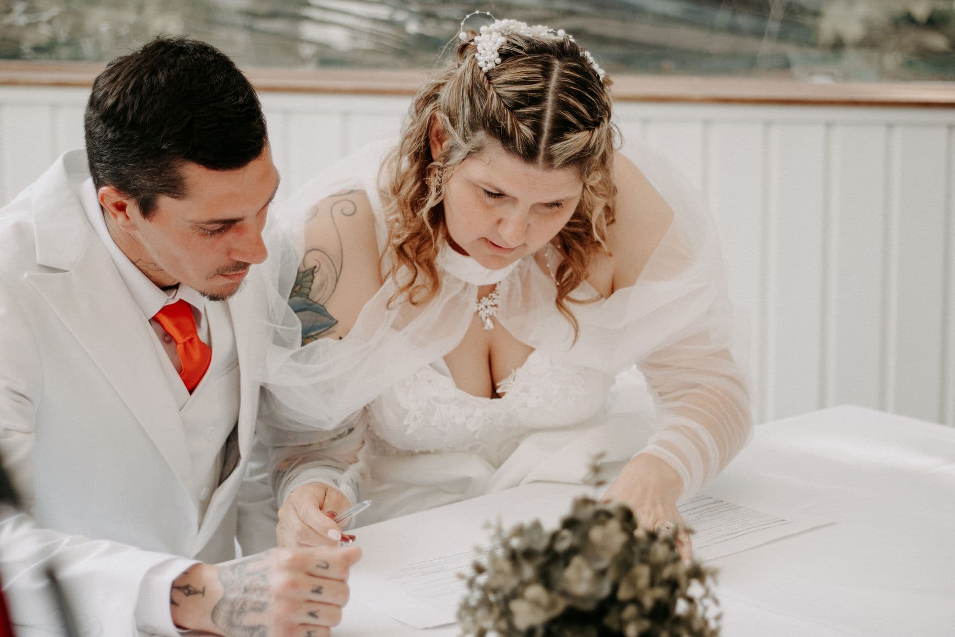 A bride and groom sign their marriage certificate during a beautiful indoor wedding ceremony.
