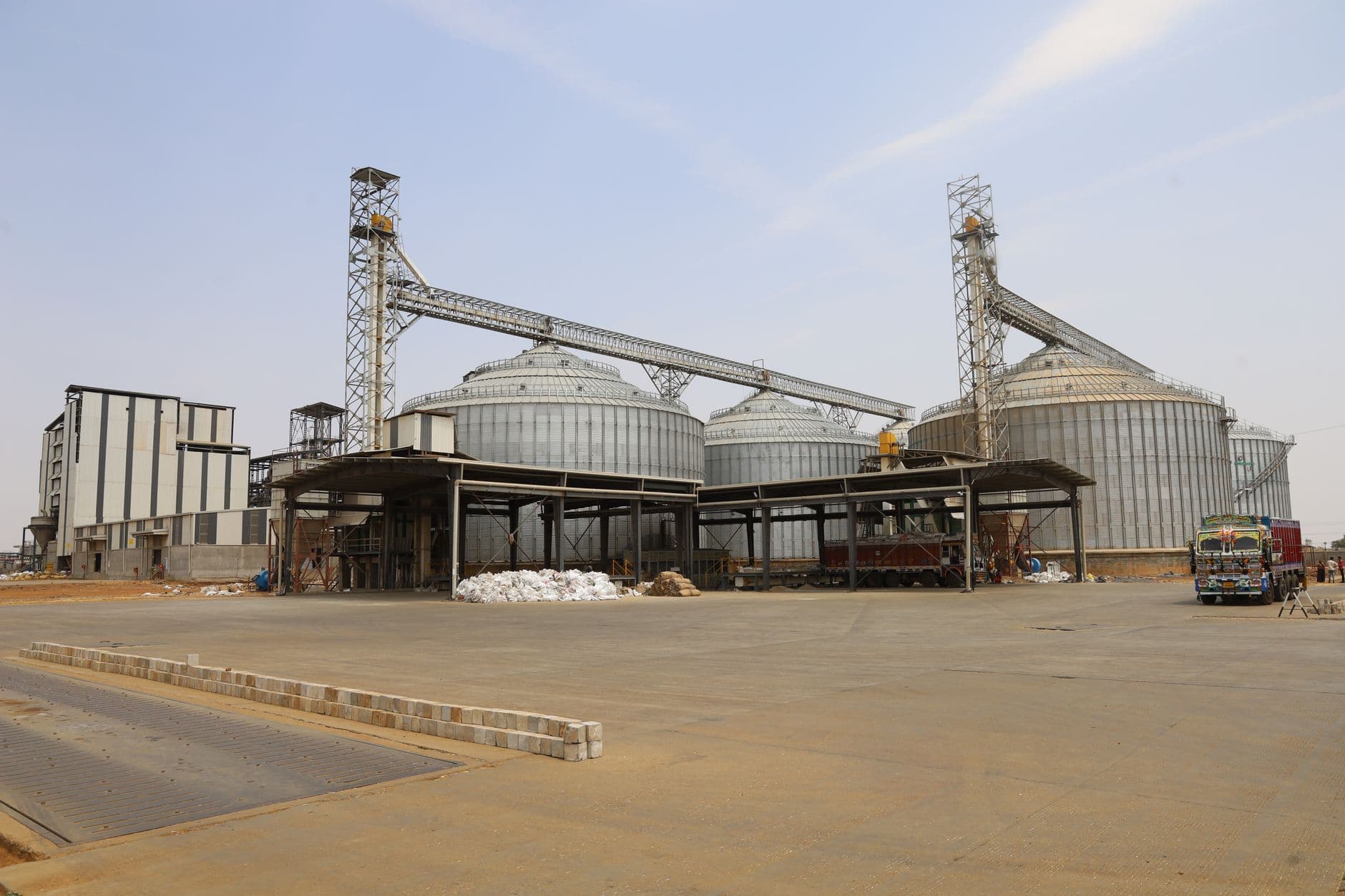 Large industrial grain silos with a truck, clear sky, and spacious outdoor area.
