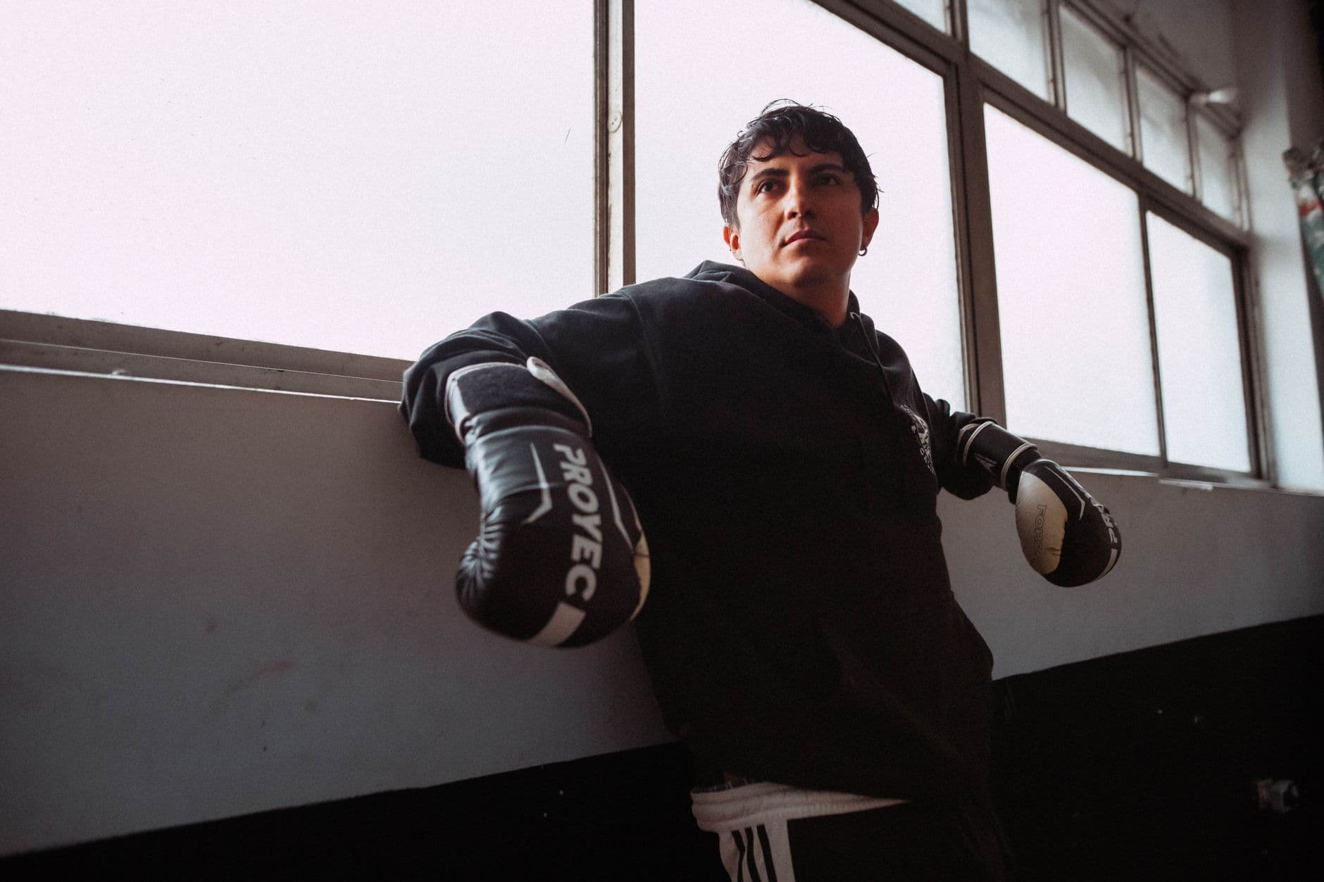 A young boxer in black gear taking a break in a Buenos Aires gym. Strong determination visible.