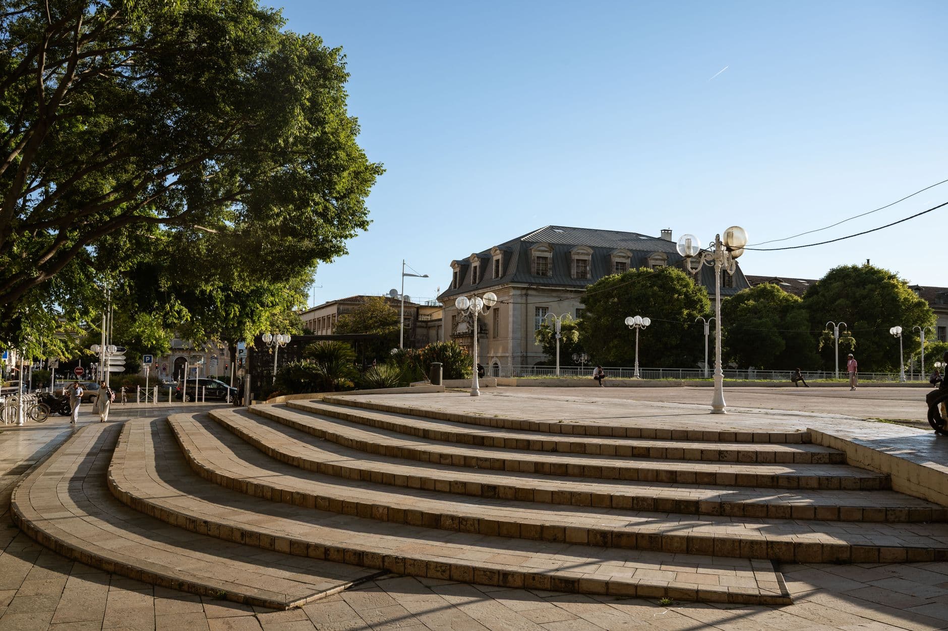 Charming stone steps and lush trees frame a historic plaza in Toulon, France, under clear skies.
