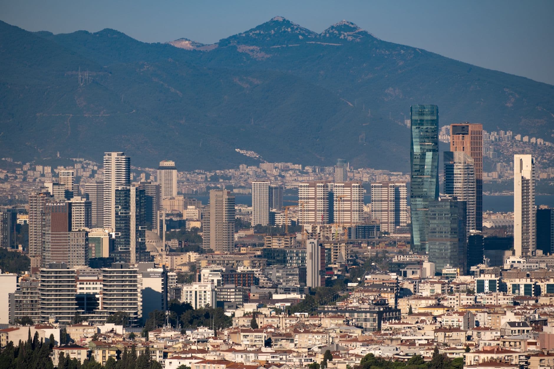 Aerial view of Izmir's modern skyline with mountains, capturing Turkey's urban landscape.