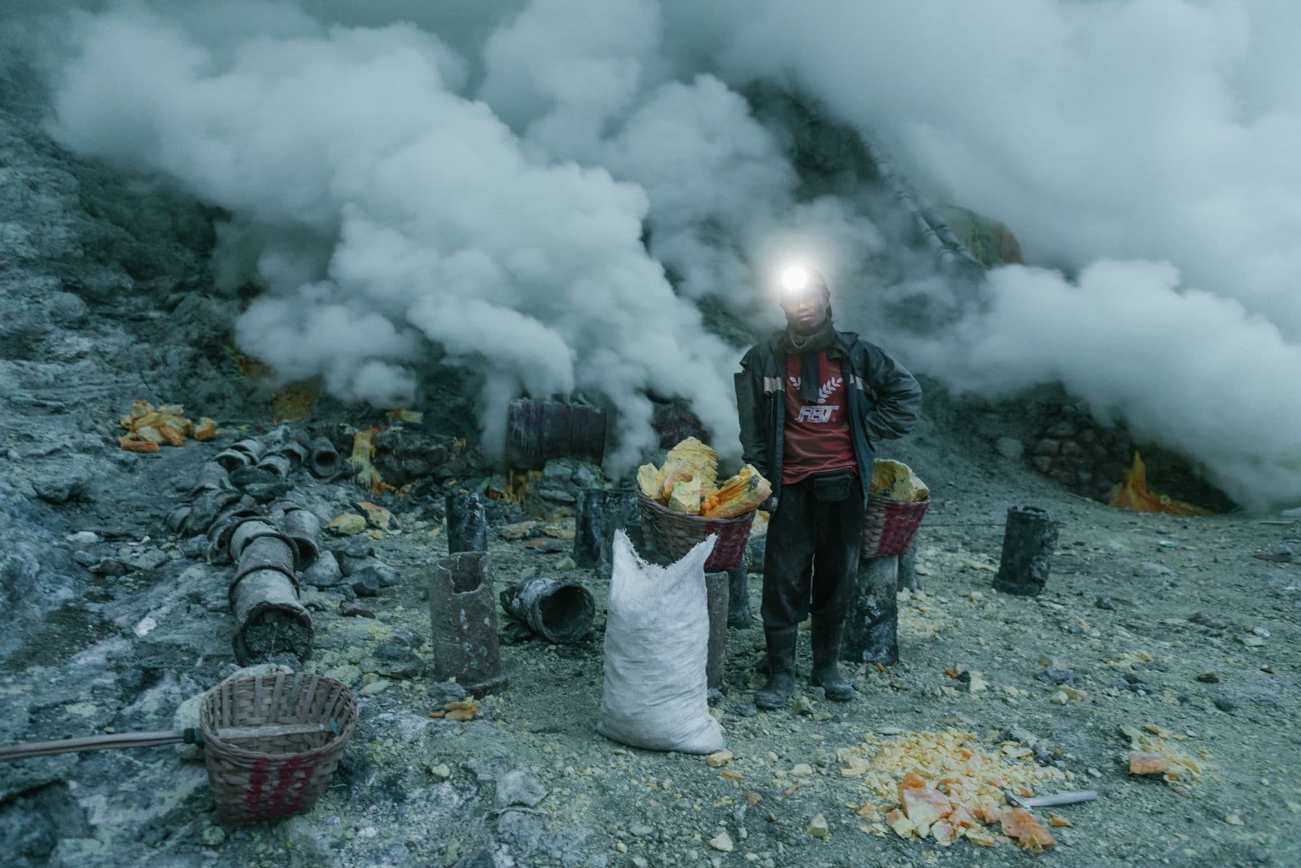 A sulfur miner stands with baskets of sulfur in a smoky volcanic mine. Dramatic industrial scene.
