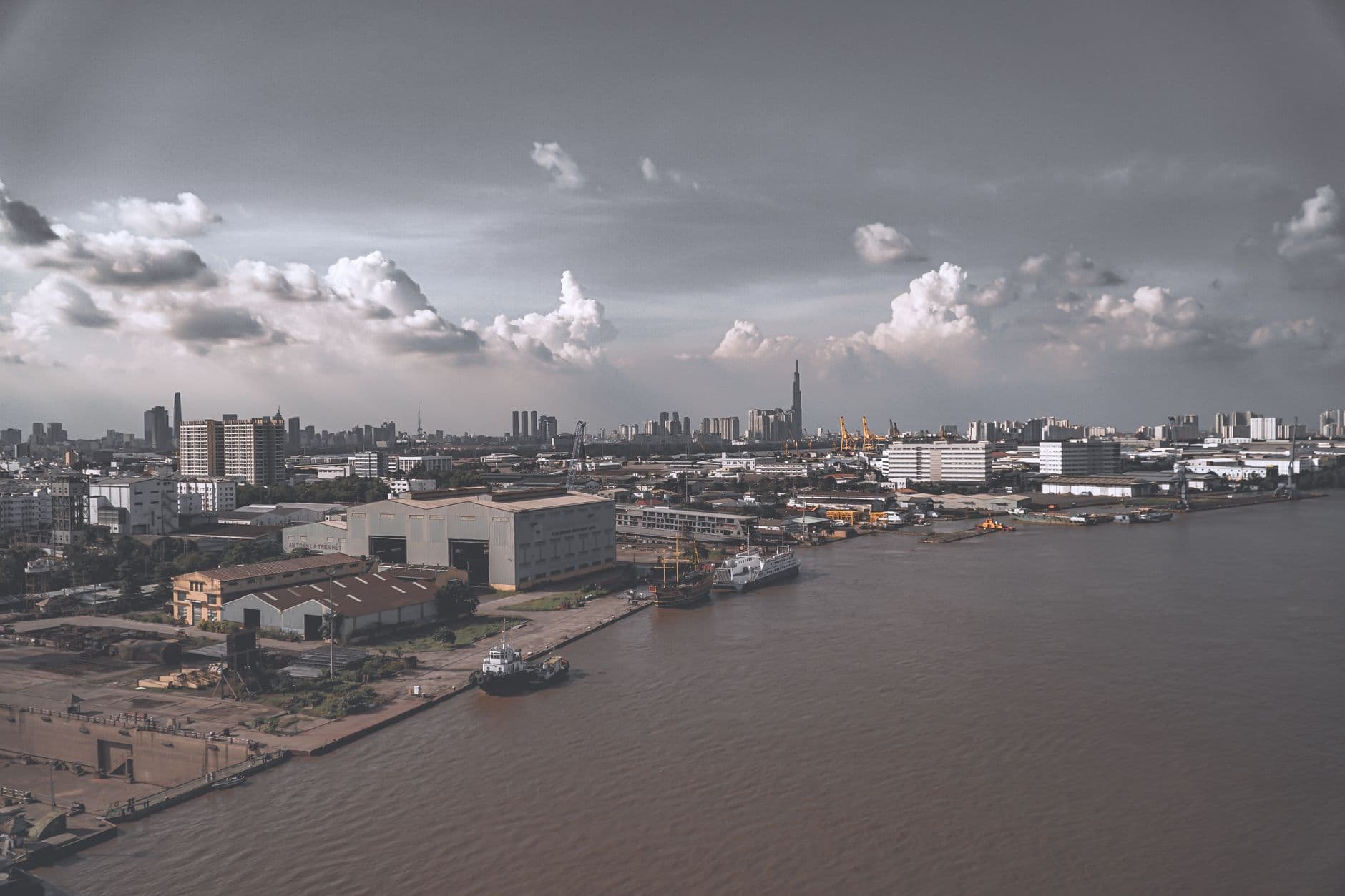 Aerial shot of a bustling urban harbor with ships and buildings under a cloudy sky.