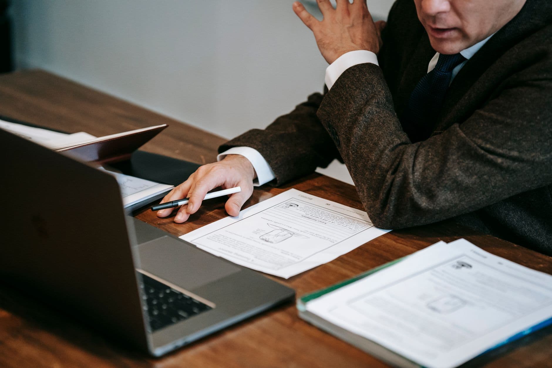 A business professional in formal attire analyzing documents and using a laptop for work indoors.