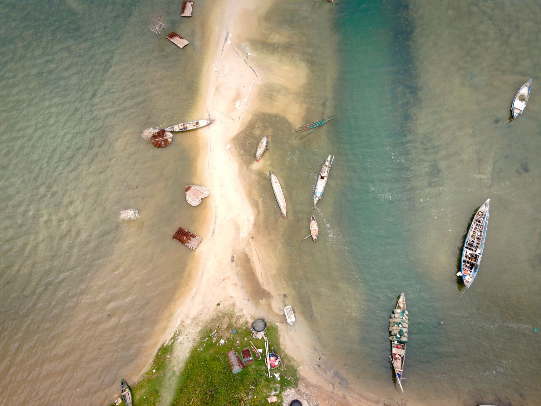 Drone shot of a sandy beach with scattered boats along the coastline.