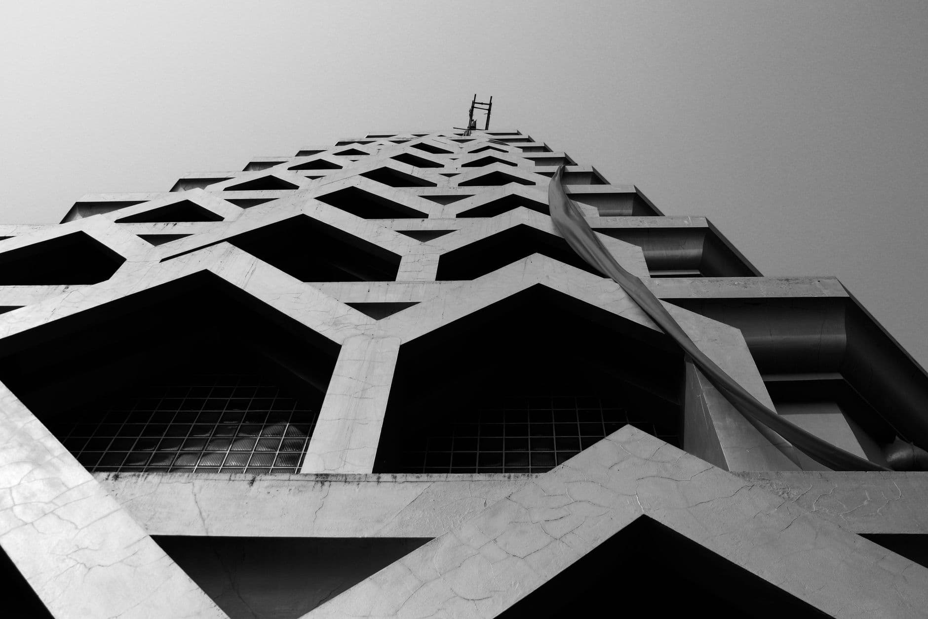 Black and white low angle exterior of contemporary high rise building with geometric symmetrical shapes under gray sky