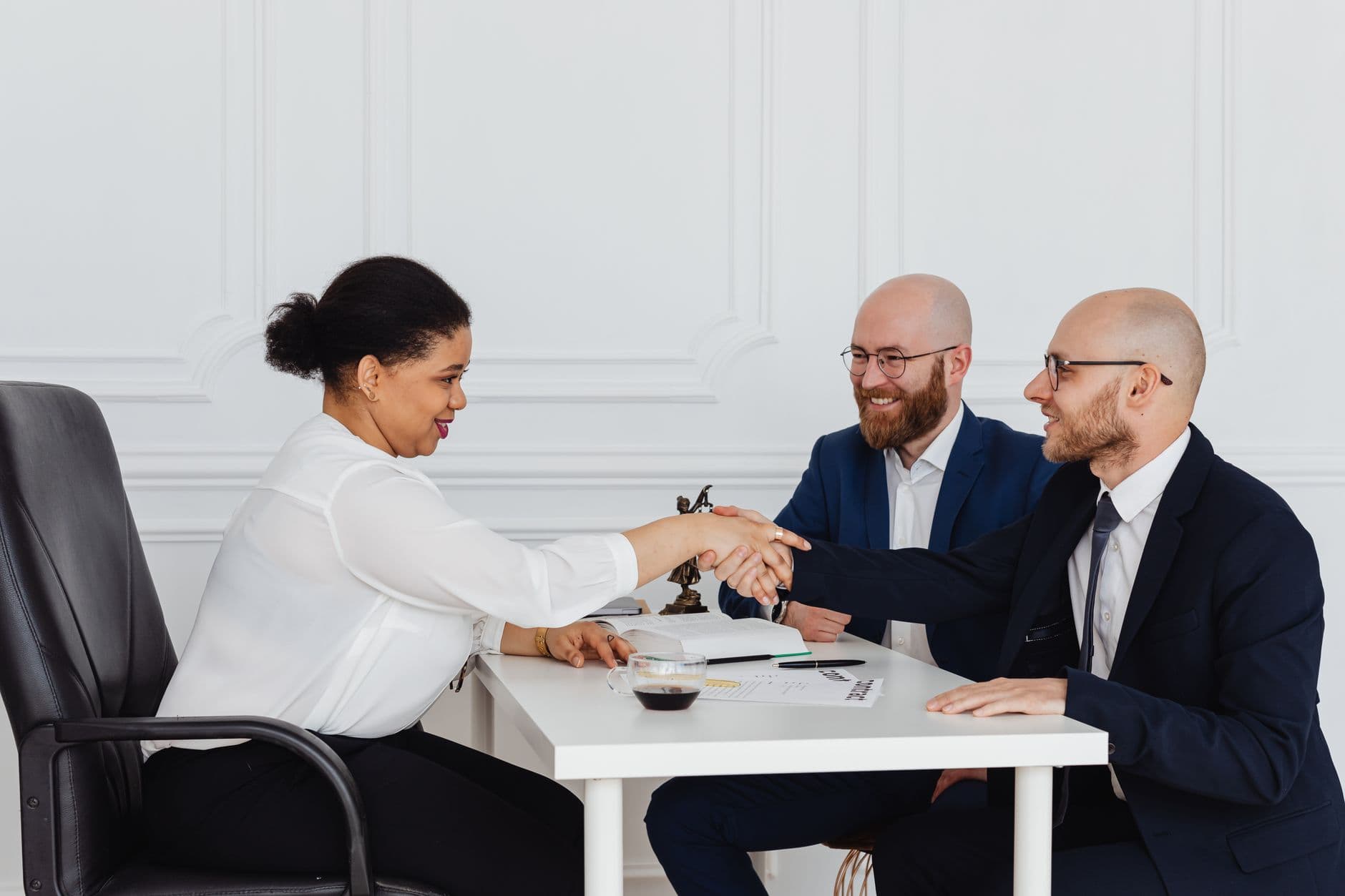 Business meeting with diverse professionals in office attire shaking hands.