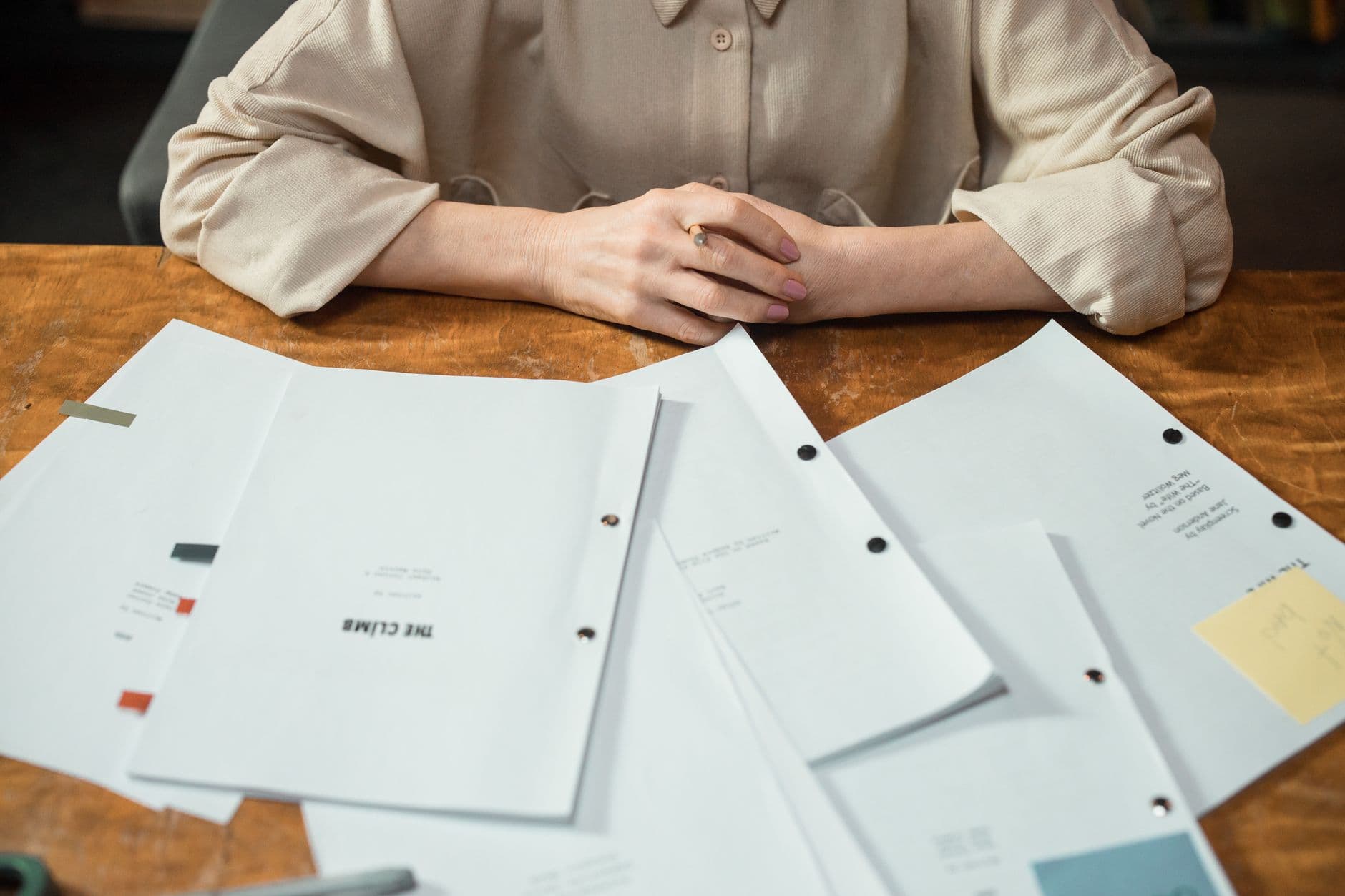 Close-up of a woman's hands with business documents on a wooden desk in an office setting.