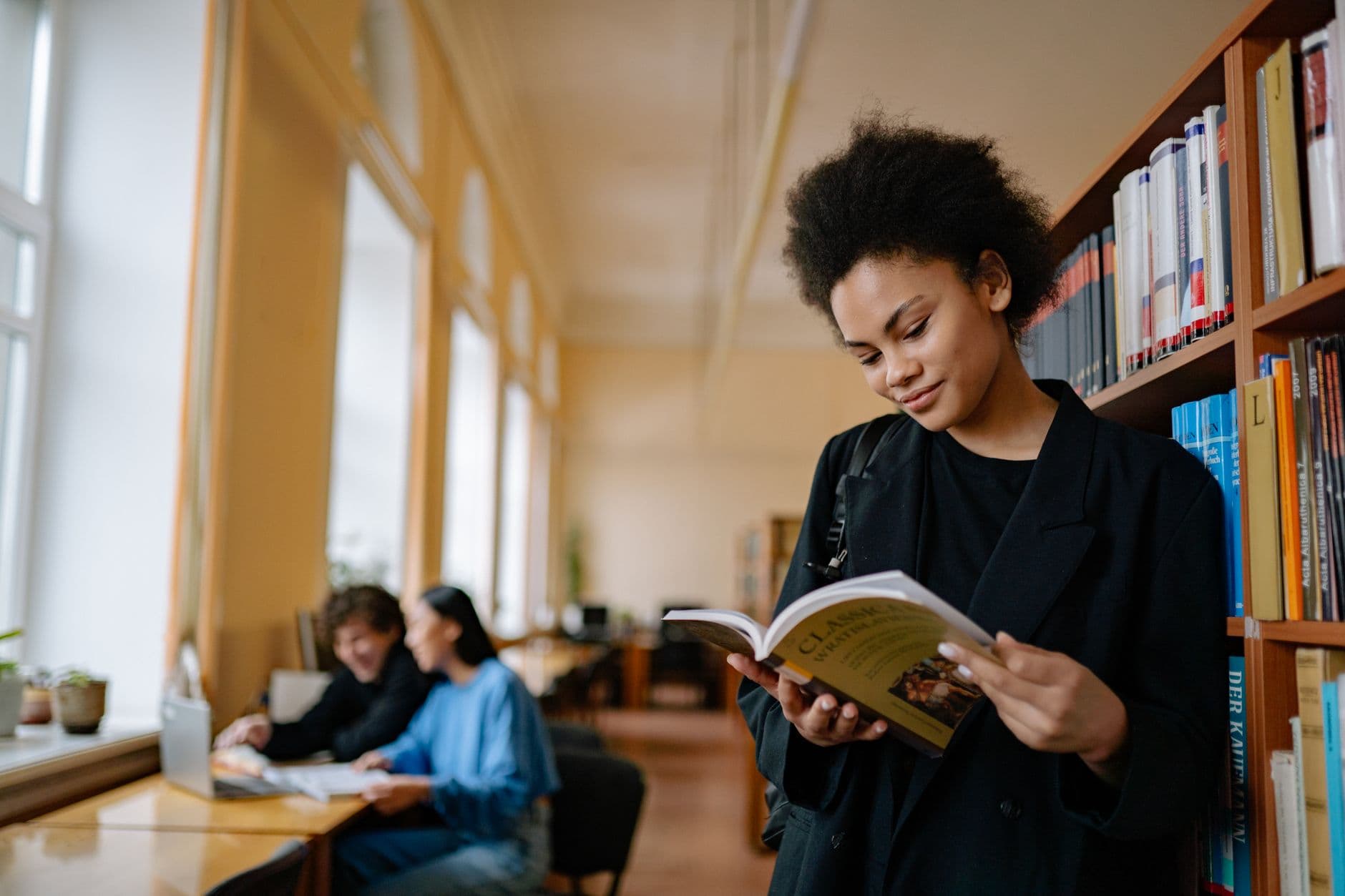 A young woman reads a book in a serene library environment, showcasing a focused academic atmosphere.