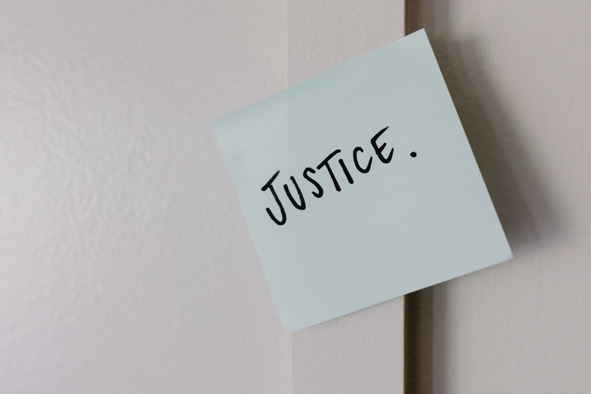 A sticky note with handwritten 'Justice' message on a white wall.