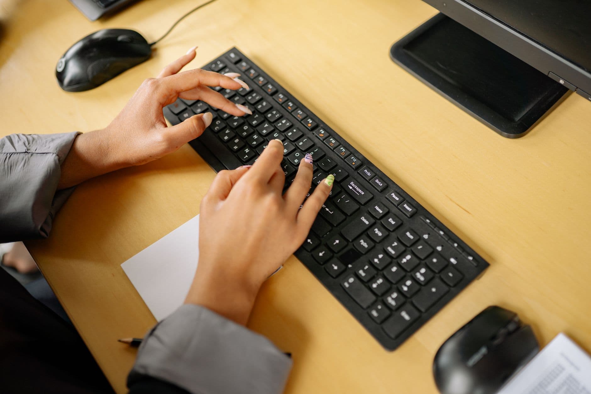 Hands typing on a keyboard in an office environment, viewed from above.