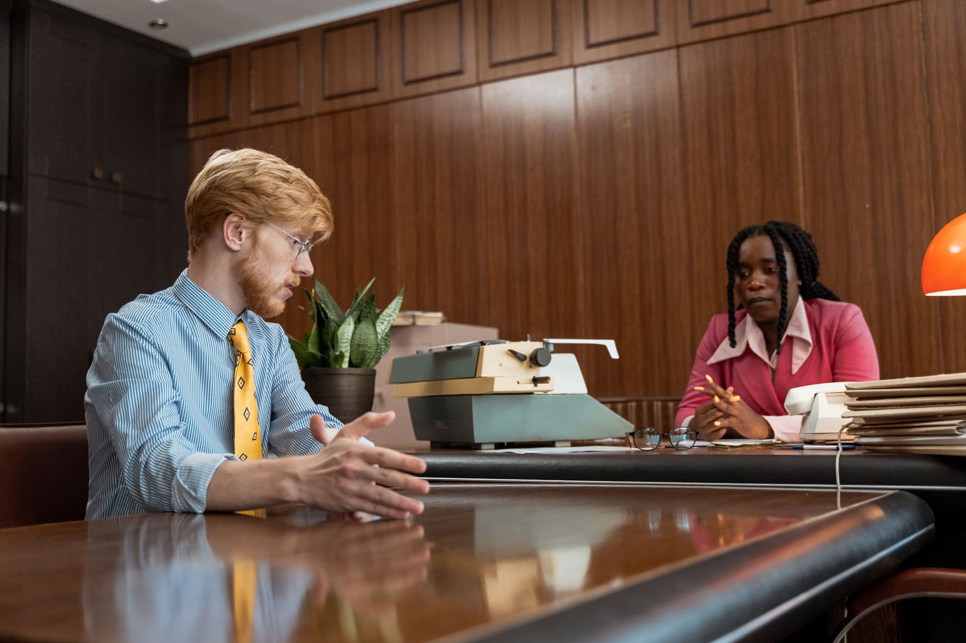Retro office with two professionals discussing over a desk and typewriter.