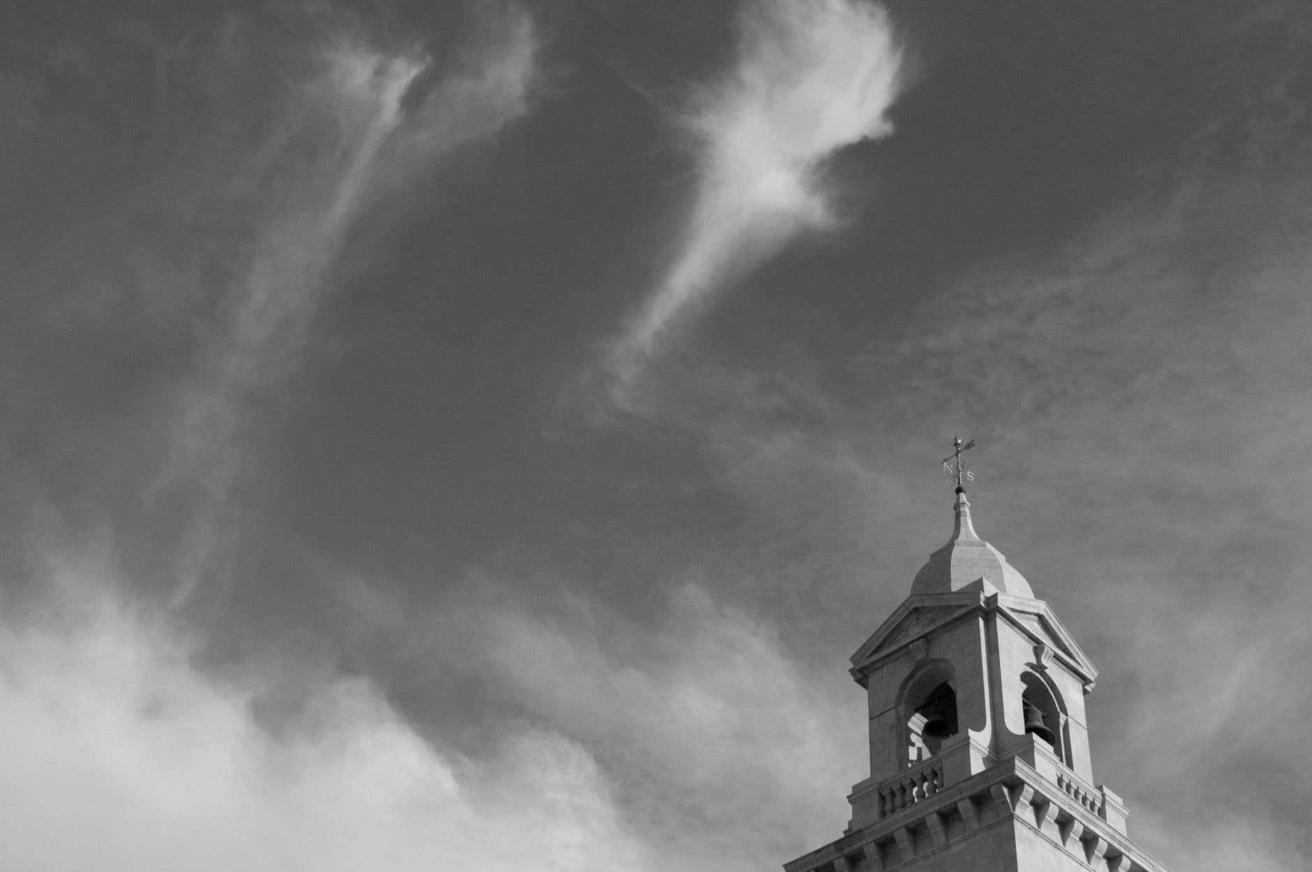 Black and white image of a church tower with dramatic clouds, emphasizing architectural beauty.