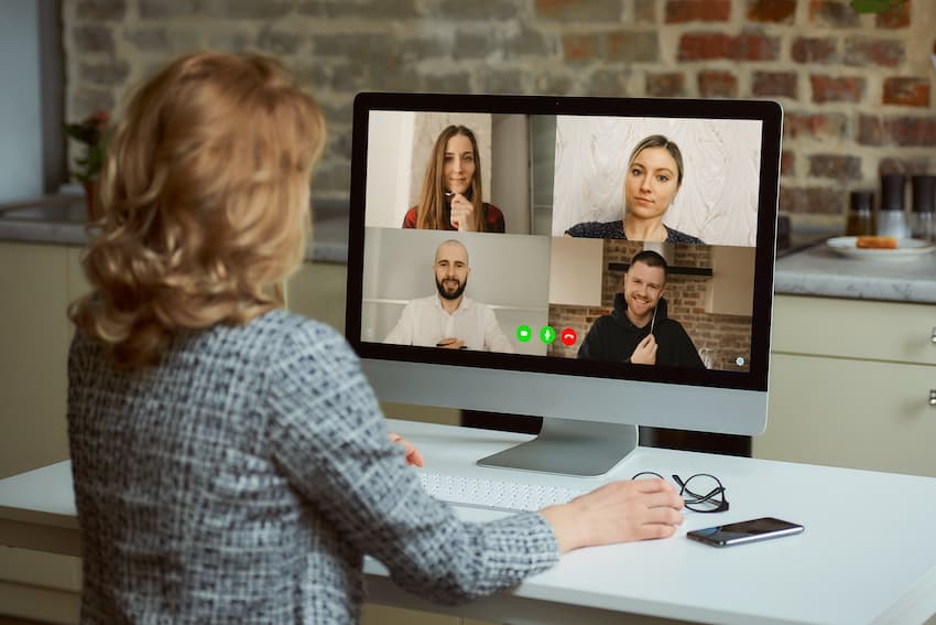 A back view of a woman who works remotely listening to reports of employees on an online briefing in her studio. A female professor listening to students on a video call on a desktop computer at home.