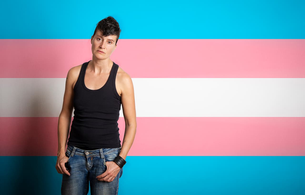 Transgender man poses with incomprehension gesture on background with transgender flag colors with copy space.